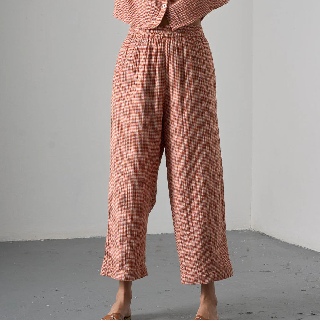 Person wearing a pink checkered outfit with wide-leg pants and a matching top against a gray background.