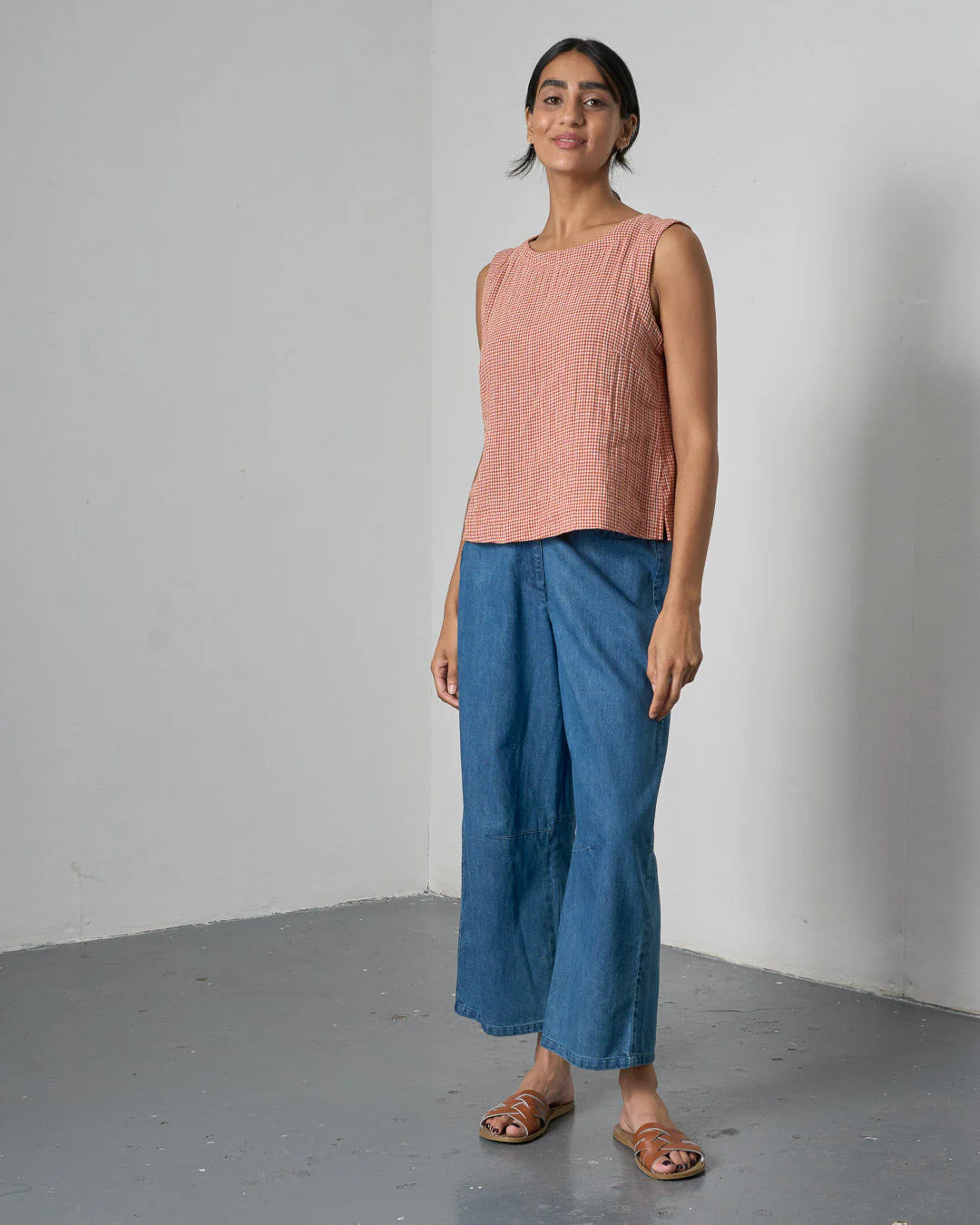 Woman wearing a pink sleeveless top and blue pants against a plain background