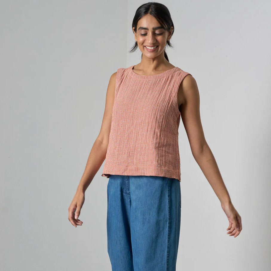 Woman wearing a pink sleeveless top and blue pants against a plain background