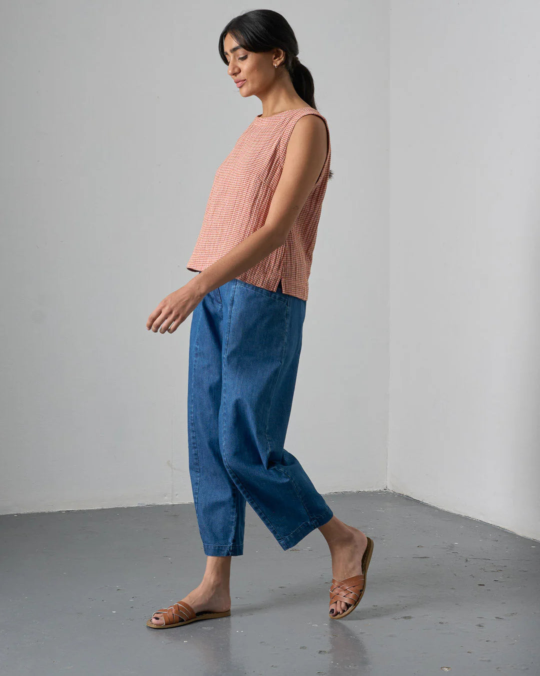 Woman wearing a pink sleeveless top and blue pants against a plain background