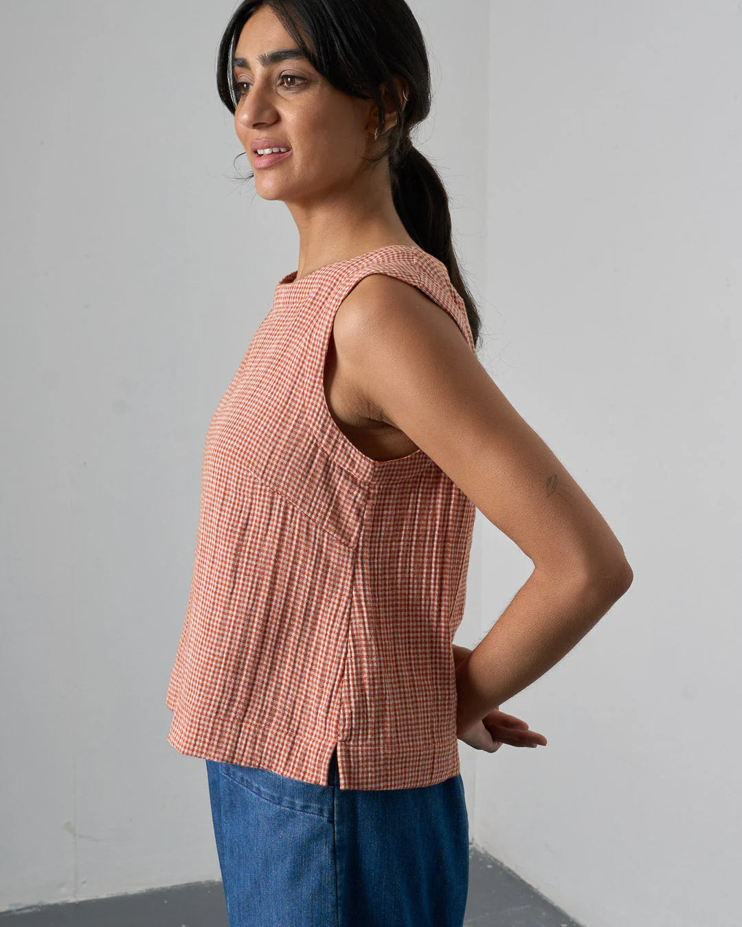 Woman wearing a sleeveless checkered top and blue jeans against a plain background