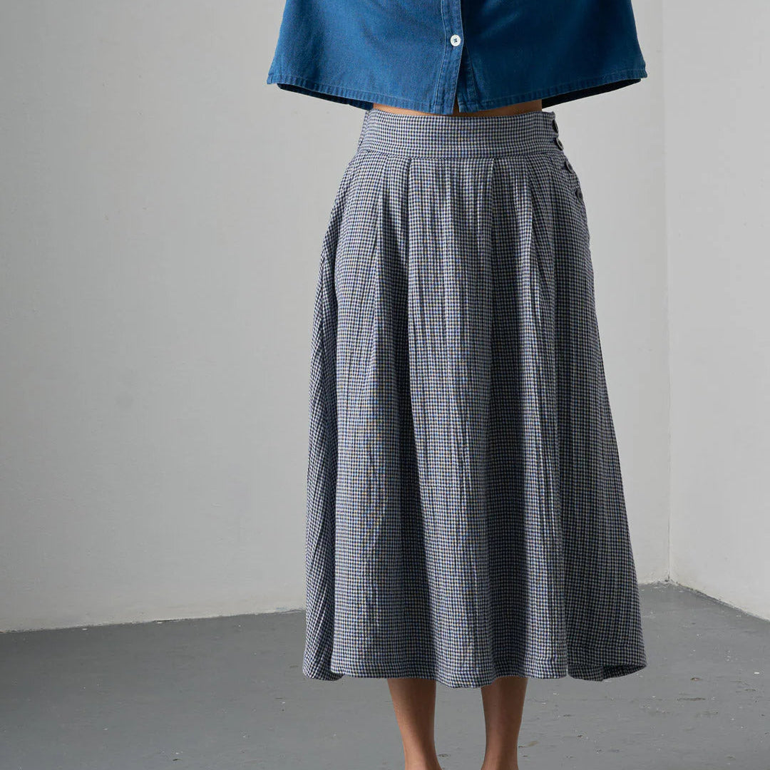 Person wearing a blue shirt and gray checkered skirt on a plain background