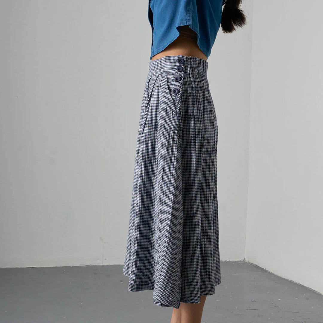 Person wearing a blue top and checkered skirt against a plain background