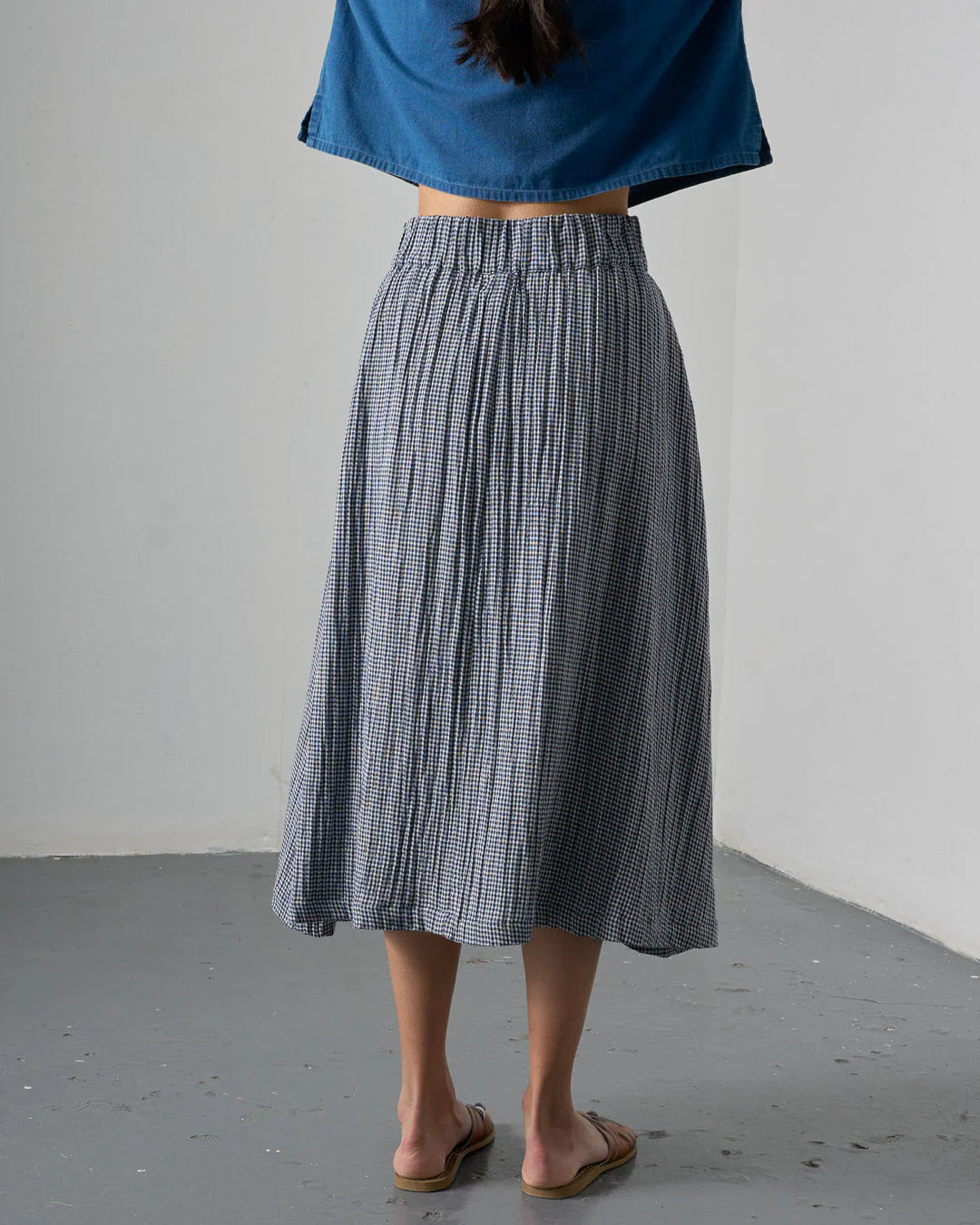 Person wearing a blue top and checkered skirt against a plain background