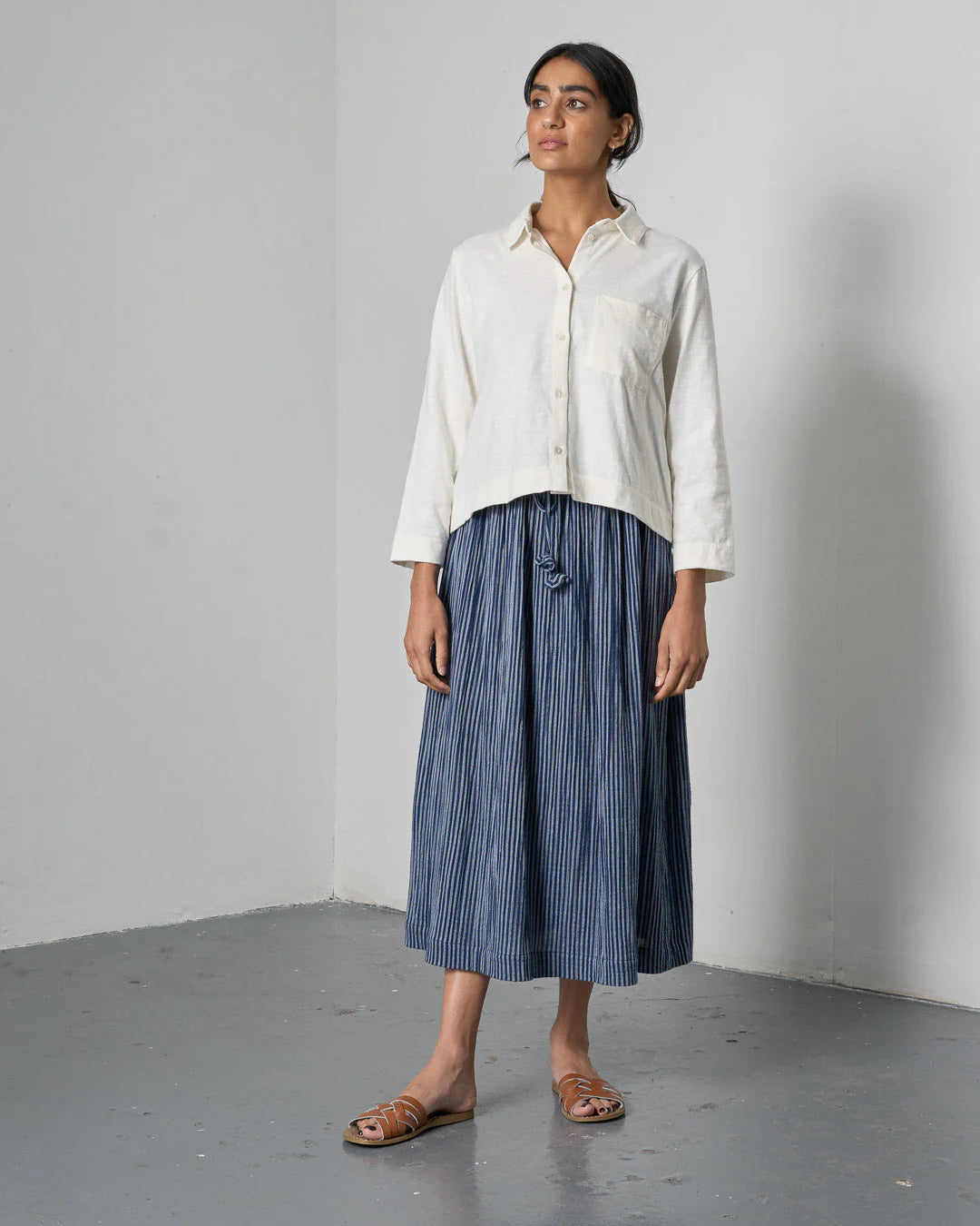 Woman wearing a white shirt and blue striped skirt against a plain background