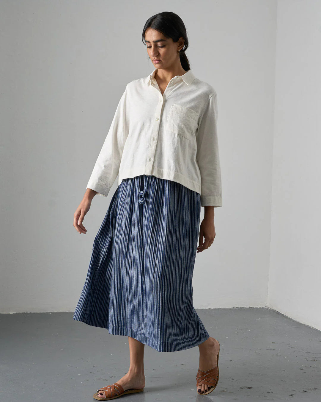 Woman wearing a white shirt and blue striped skirt against a plain background