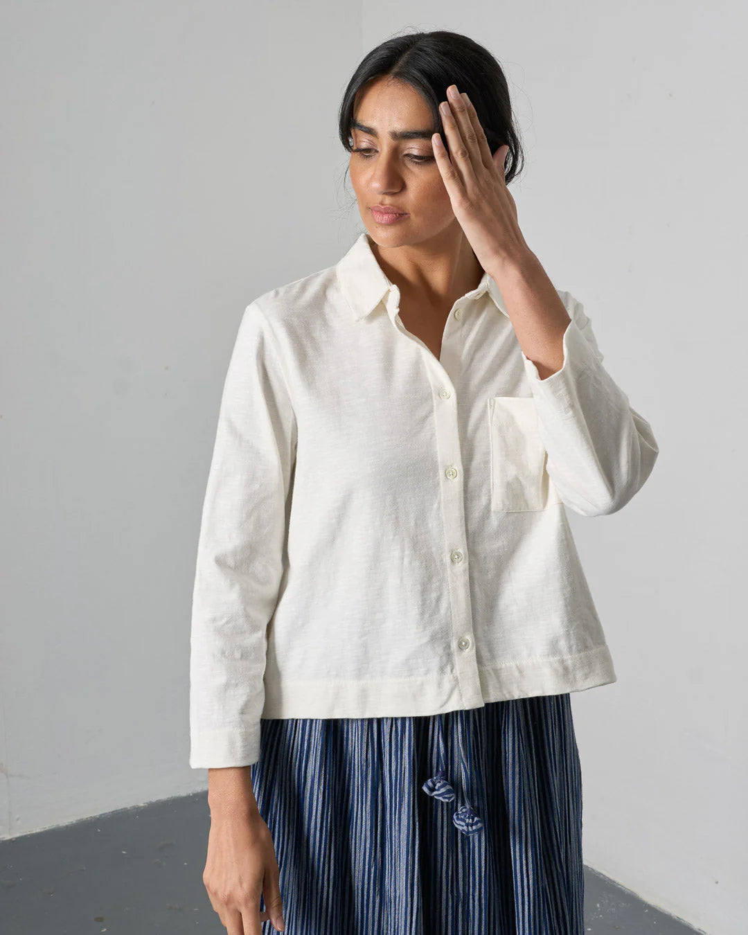 Woman wearing a white shirt over a striped dress against a plain background