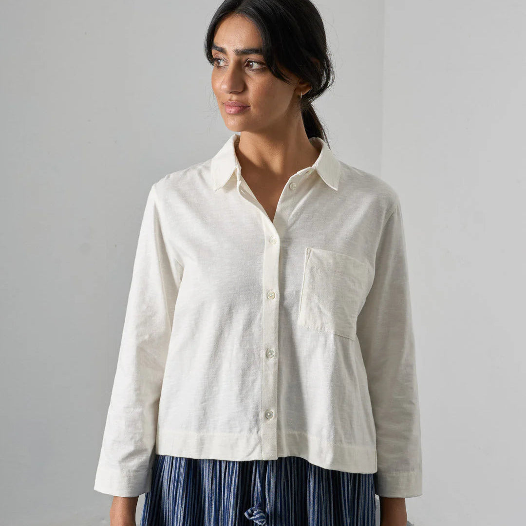 Woman wearing a white shirt with a pocket against a plain background