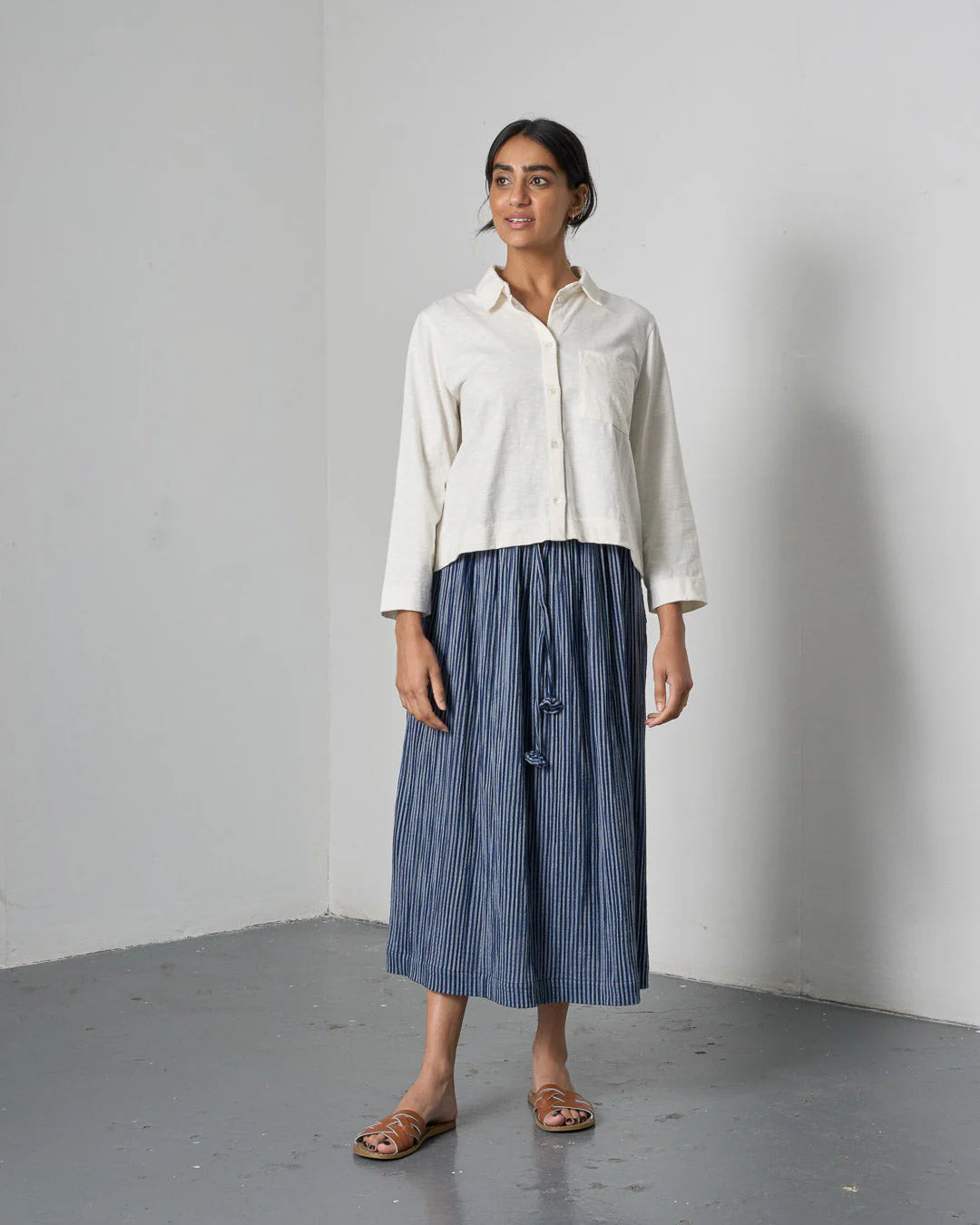 Woman wearing a white shirt and blue striped skirt against a plain background