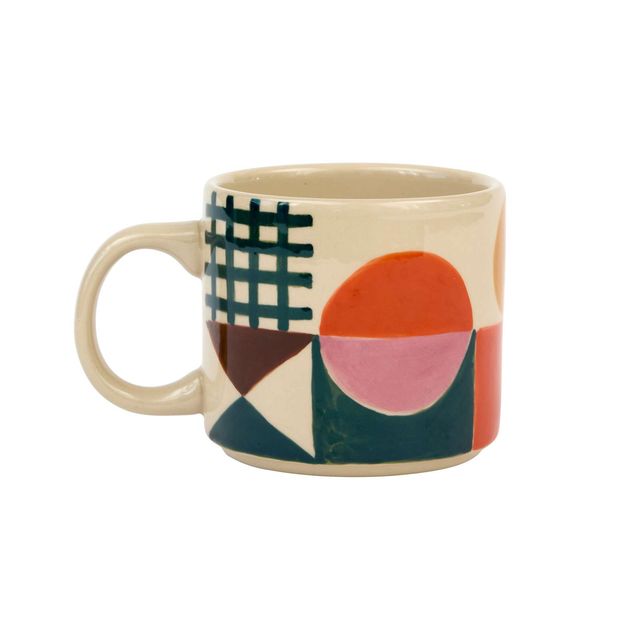 A ceramic coffee mug with a cream-colored base and a colorful geometric pattern featuring orange, pink, green, brown, and white shapes, shown on a plain white background.