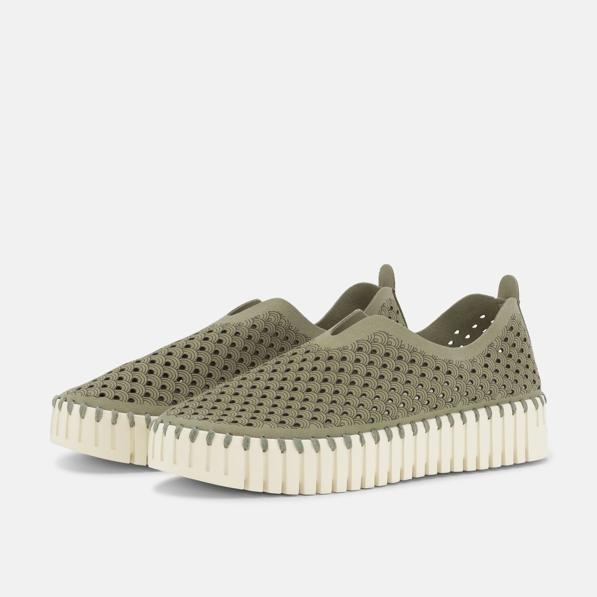 Pair of olive green slip-on shoes with a textured, patterned upper and a cream-colored, ridged sole. The pattern features