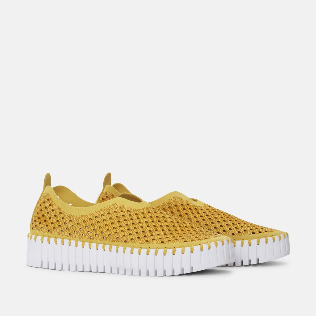 Mustard yellow slip-on shoes with a white, textured sole and a repeating wave pattern.