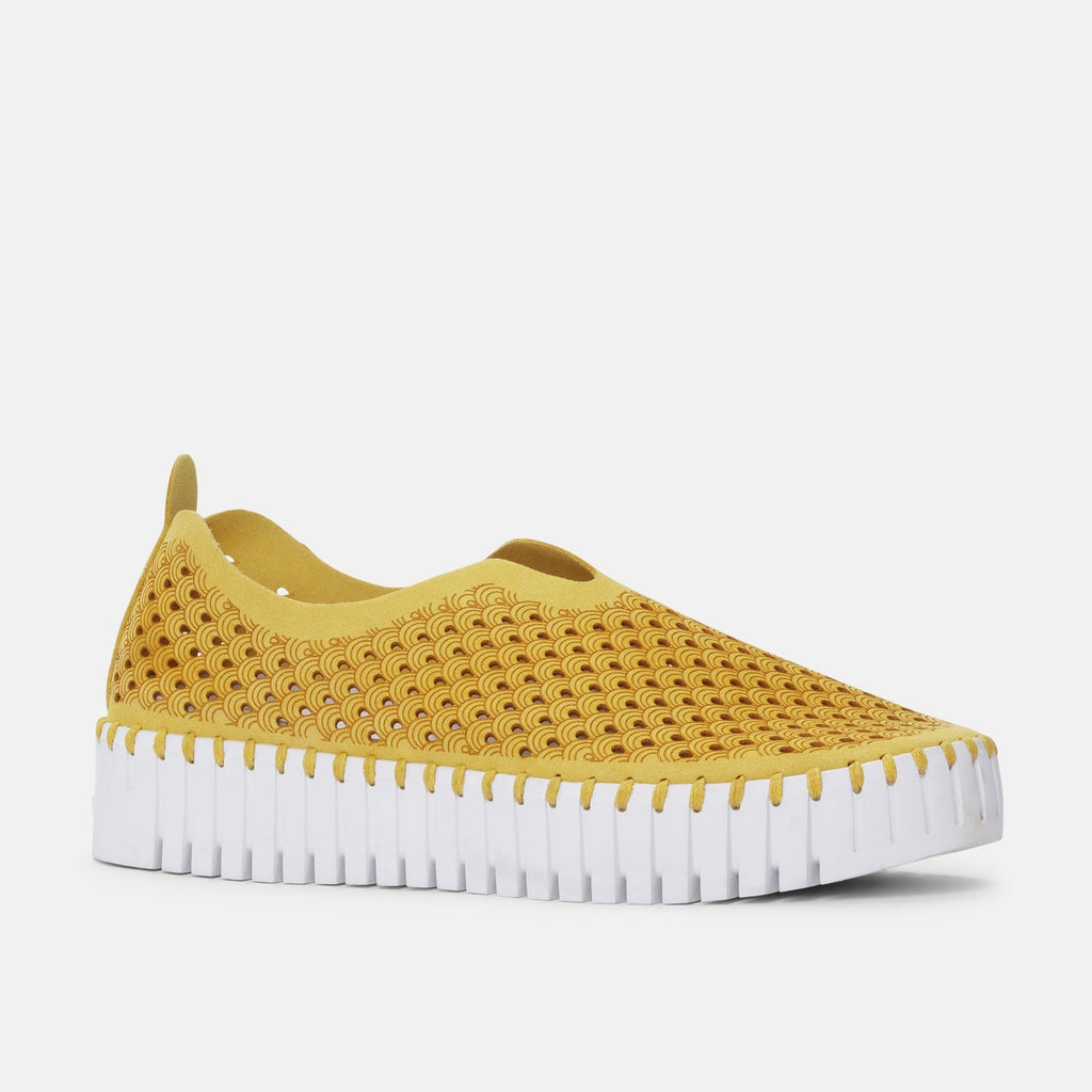 Mustard yellow slip-on shoe with a wave pattern and white, ridged sole. The upper is perforated with a repeating design.