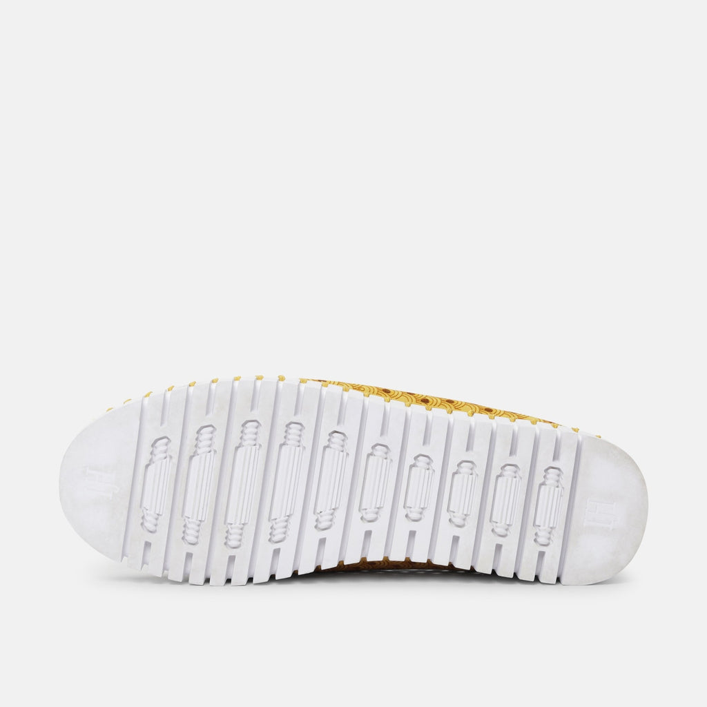 White rubber sole of a shoe with a gold and brown patterned upper. The sole features a textured tread with repeating indented
