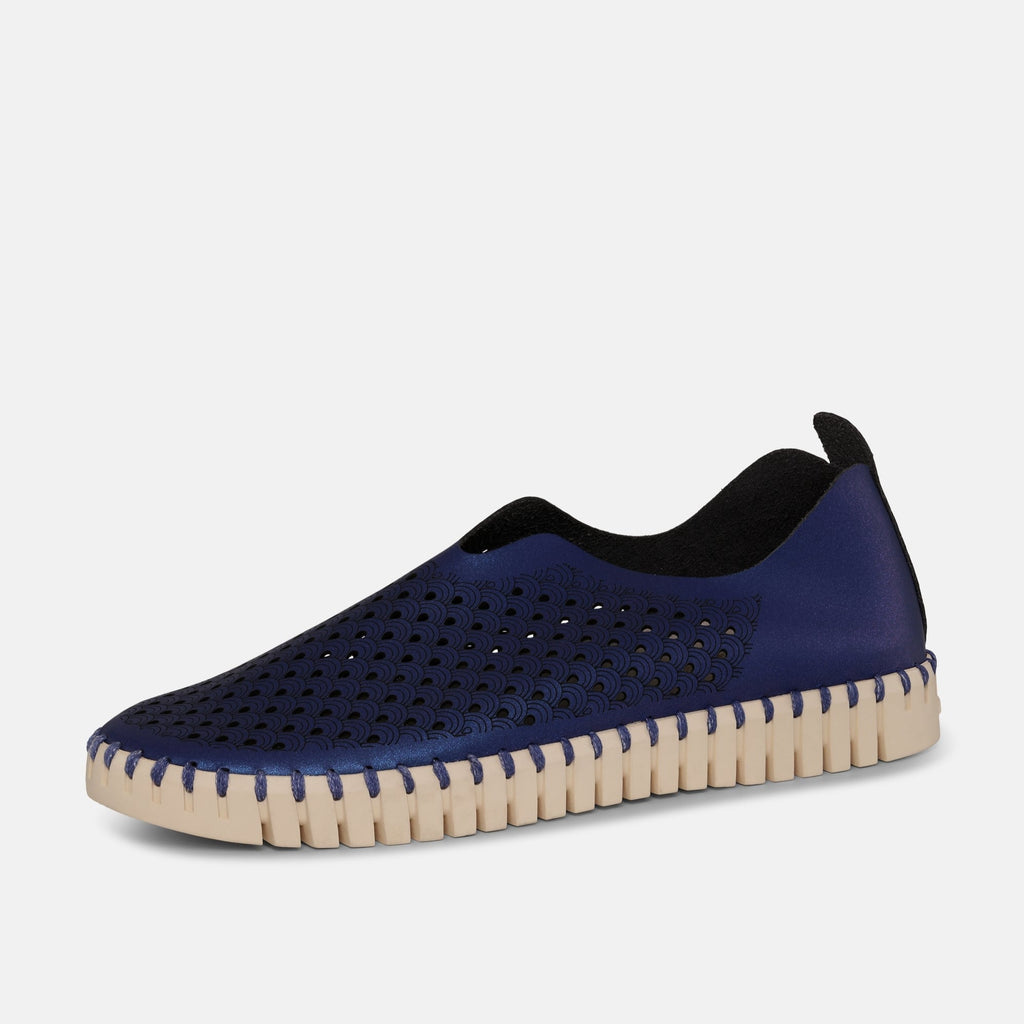 Navy blue slip-on shoe with laser-cut wave pattern, cream-colored textured sole, and dark gray fabric lining.