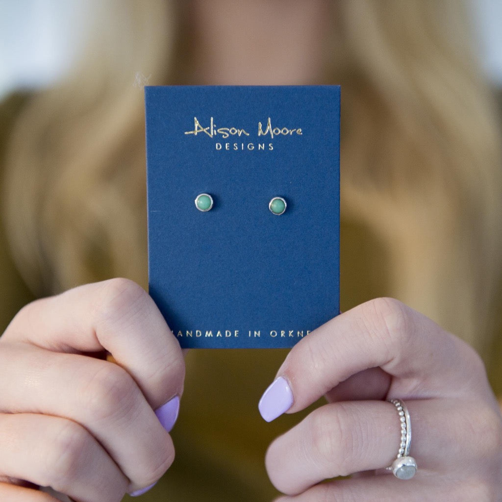 Pair of pale green gemstone stud earrings on a navy blue card.  Alison Moore Designs. Handmade in Orkney.