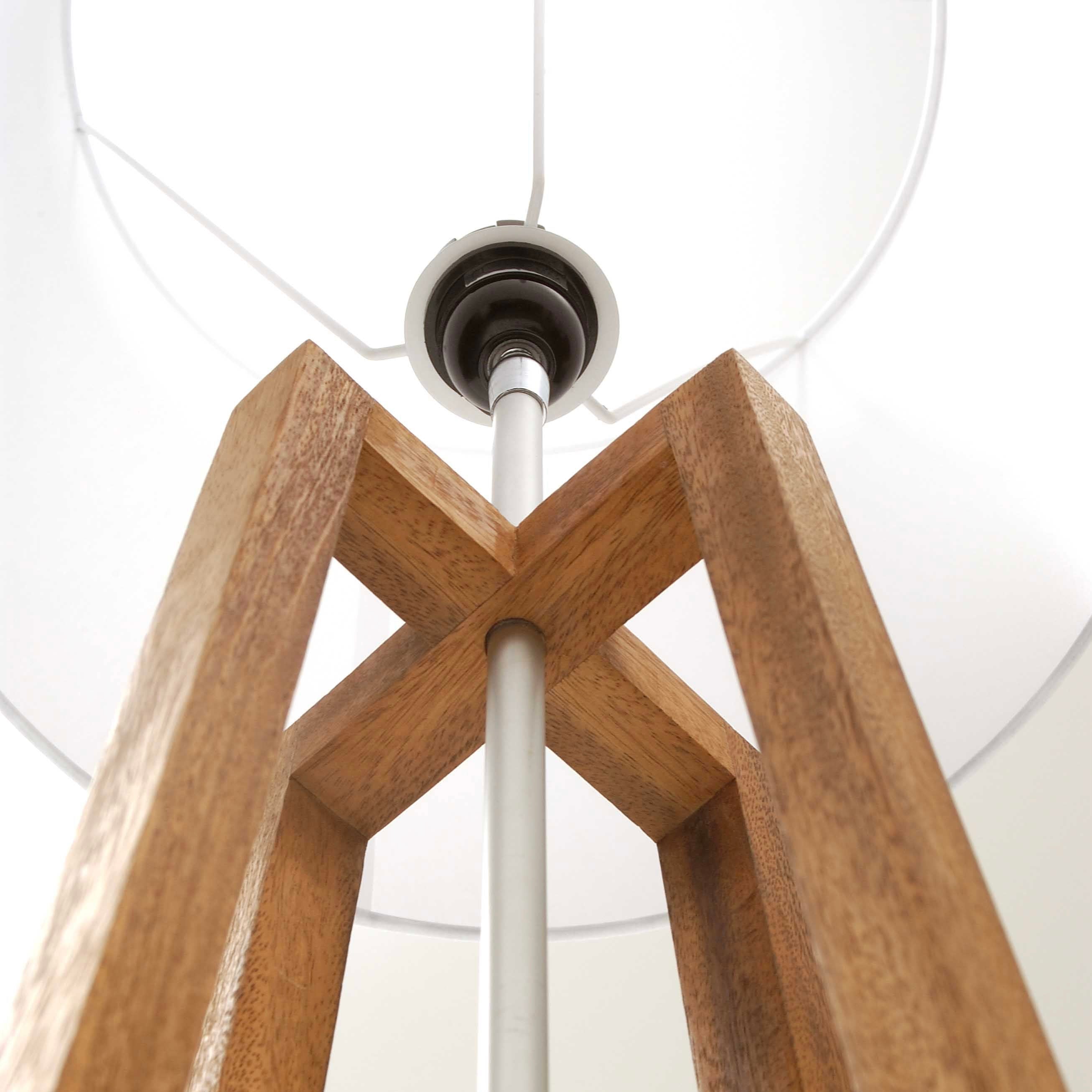 Wooden floor lamp with a white shade and a silver metal pole. The base is a light brown, square-shaped wooden structure.