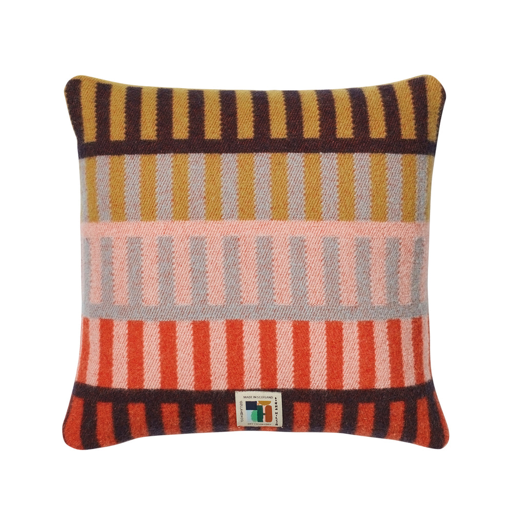 Colorful striped cushion by Donna Wilson featuring gold, brown, gray, pink, and red tones.