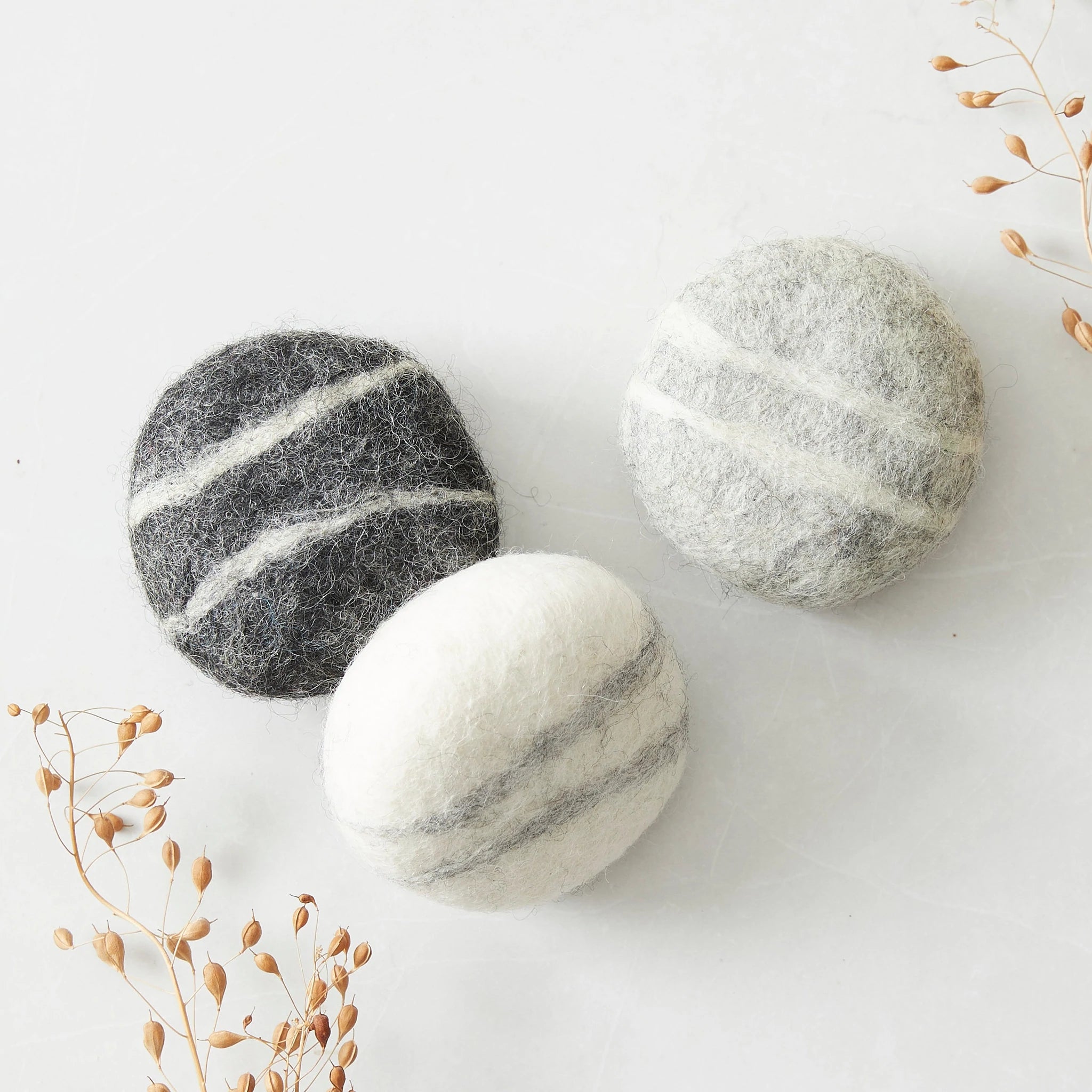 Three round felted wool dryer balls in gray, dark gray, and white with contrasting stripes.