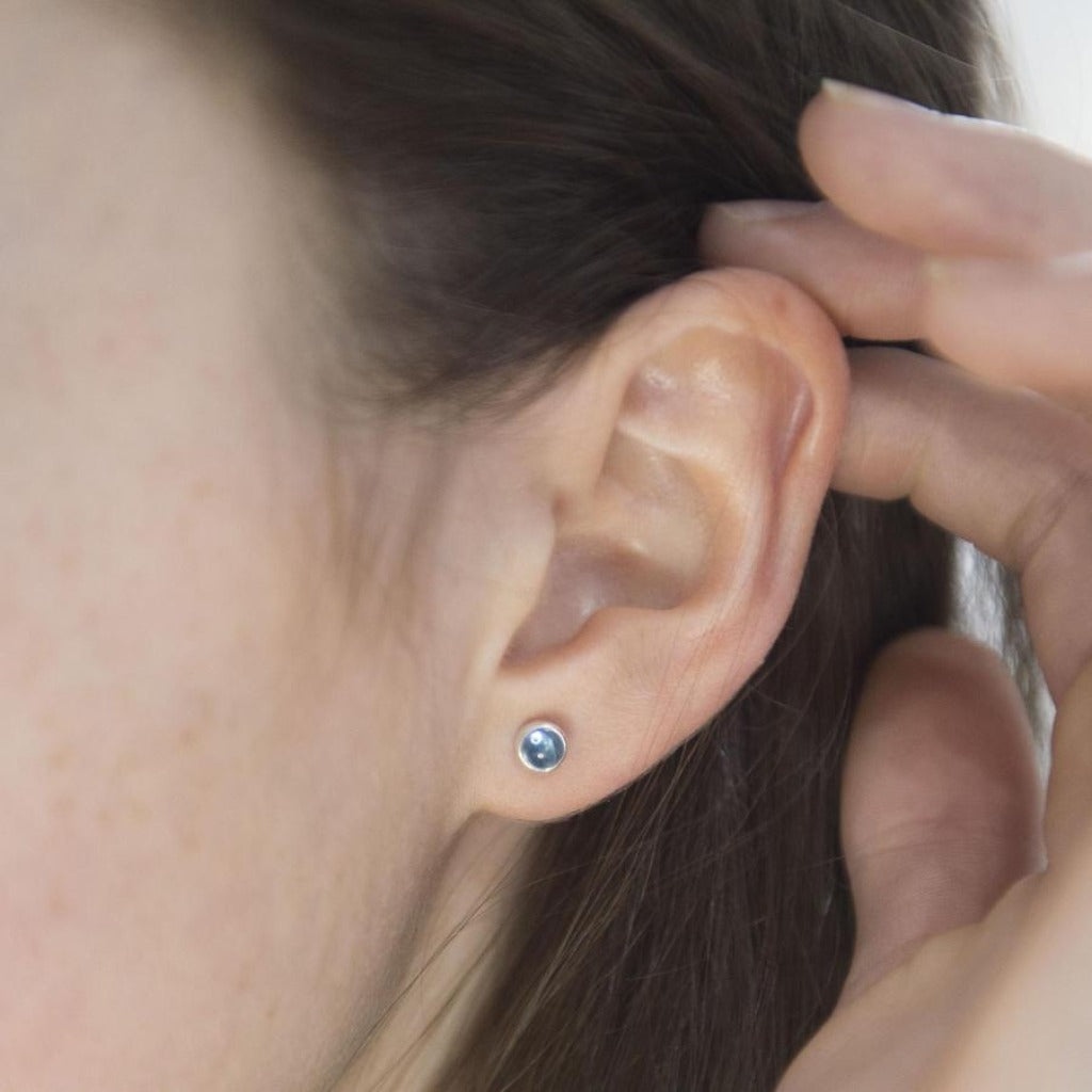 Small, round blue gemstone stud earrings in silver settings.