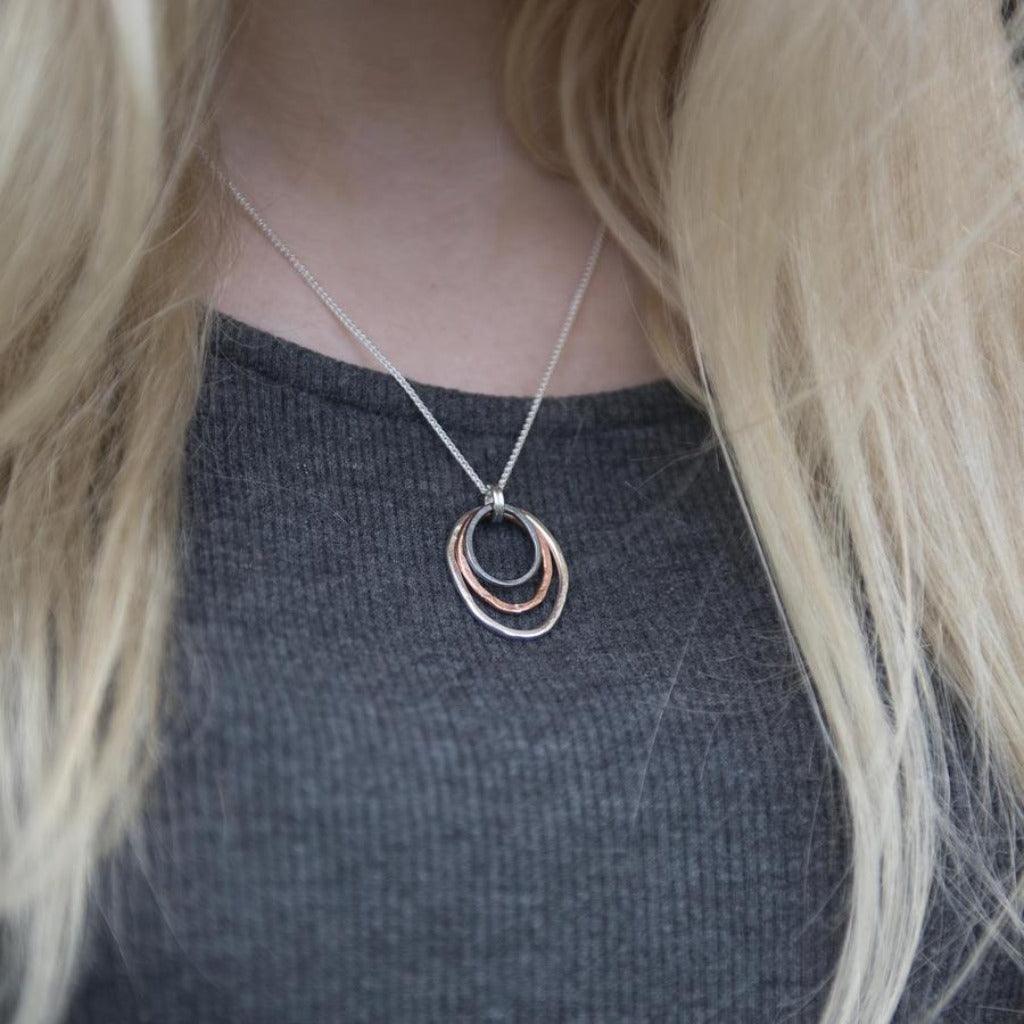 Silver chain necklace with a pendant featuring three overlapping hammered metal circles in silver, dark gray, and copper