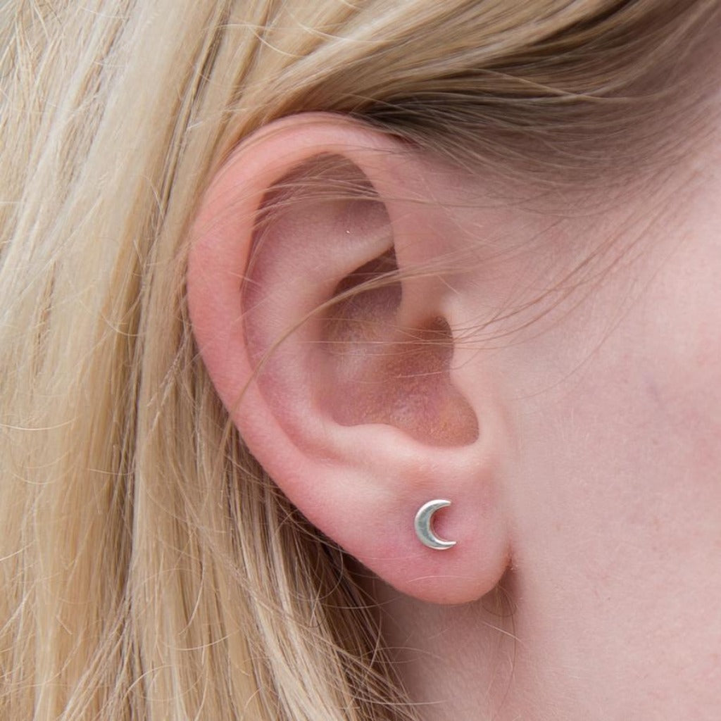 Silver crescent moon stud earrings in a person's ear.