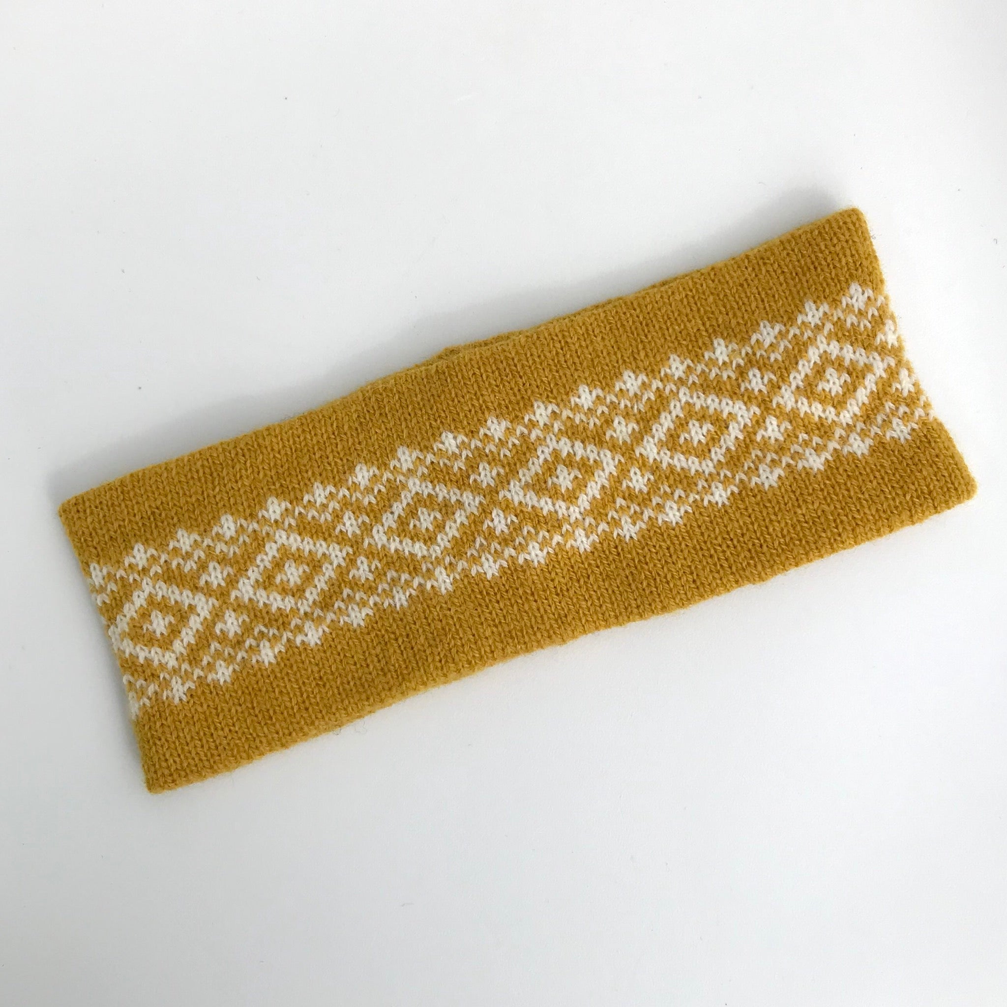 Mustard yellow knitted headband with a white geometric pattern.