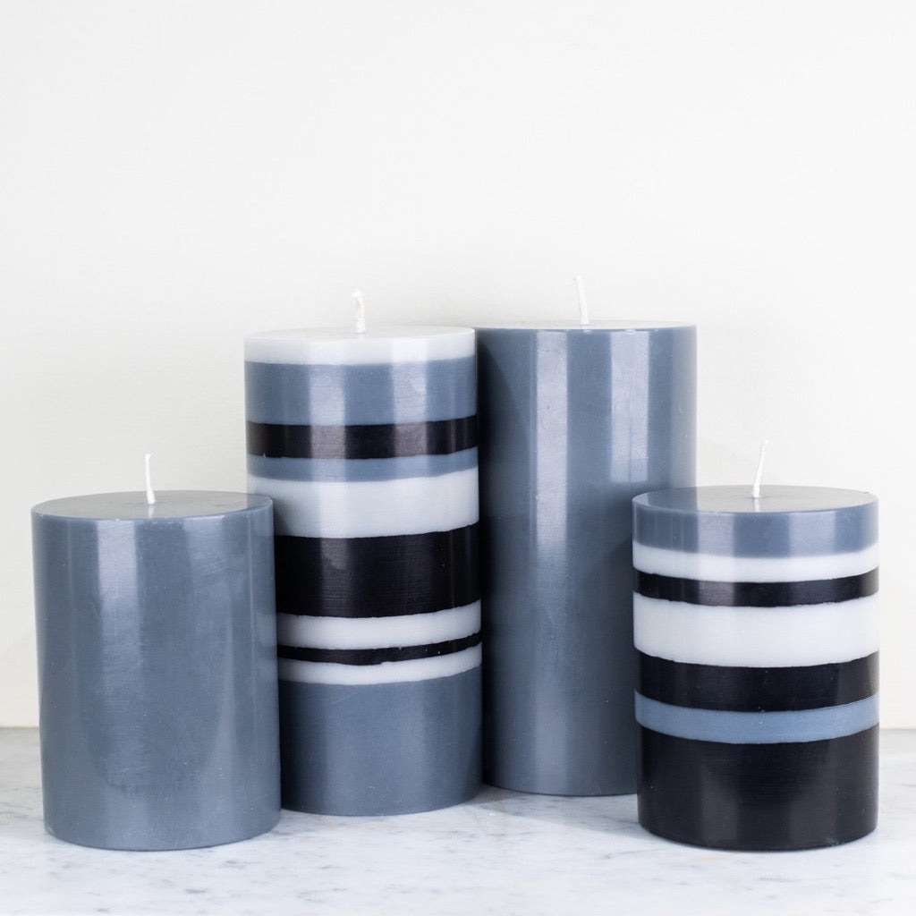 Four cylindrical candles in shades of gray and black with horizontal stripes.