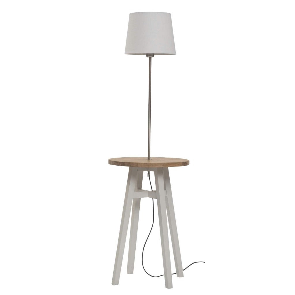 Floor lamp with a light gray fabric shade mounted on a white side table with a light wood top.