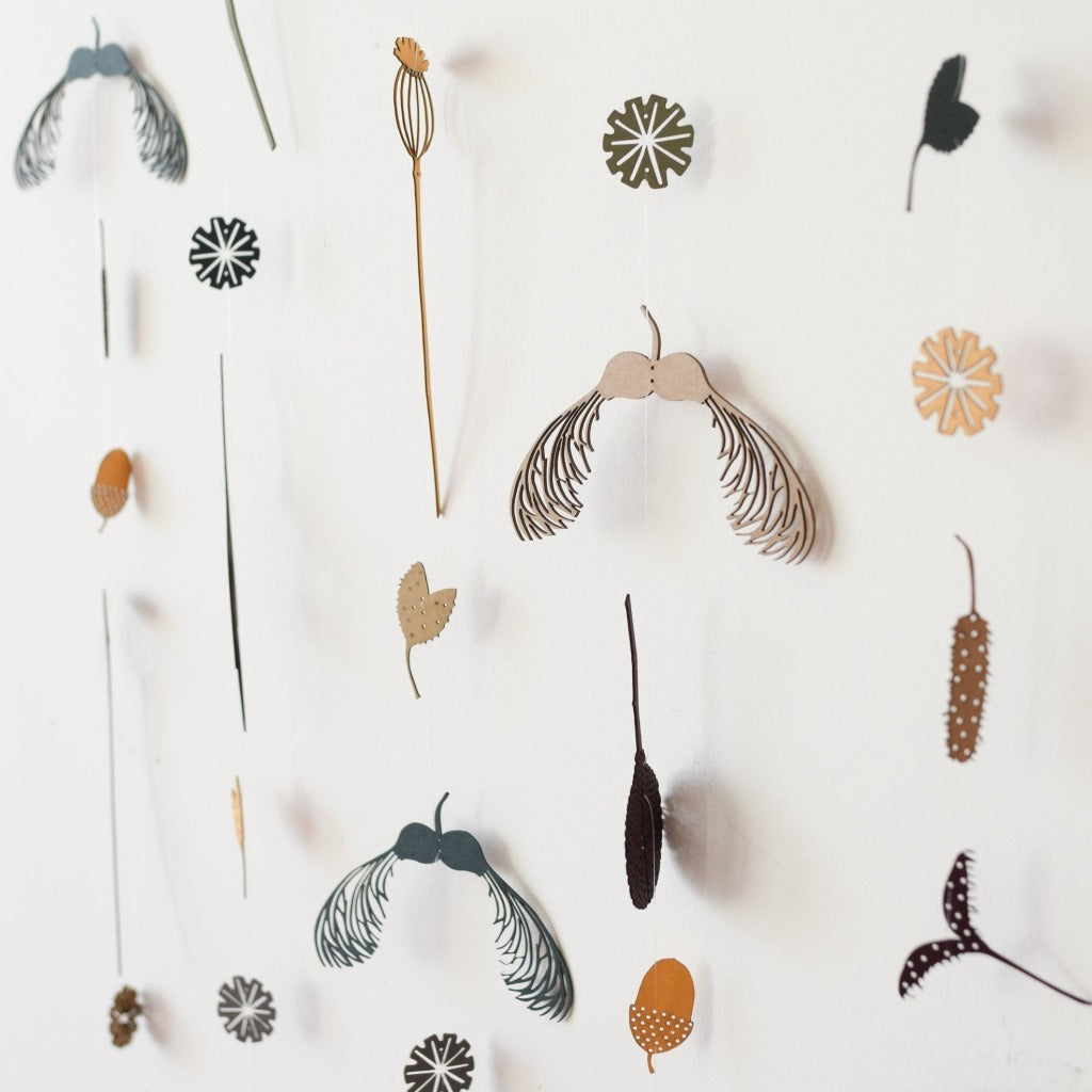 Collection of laser-cut wood botanical wall hangings.  Designs include maple seeds, flowers, and leaves in muted earth tones.