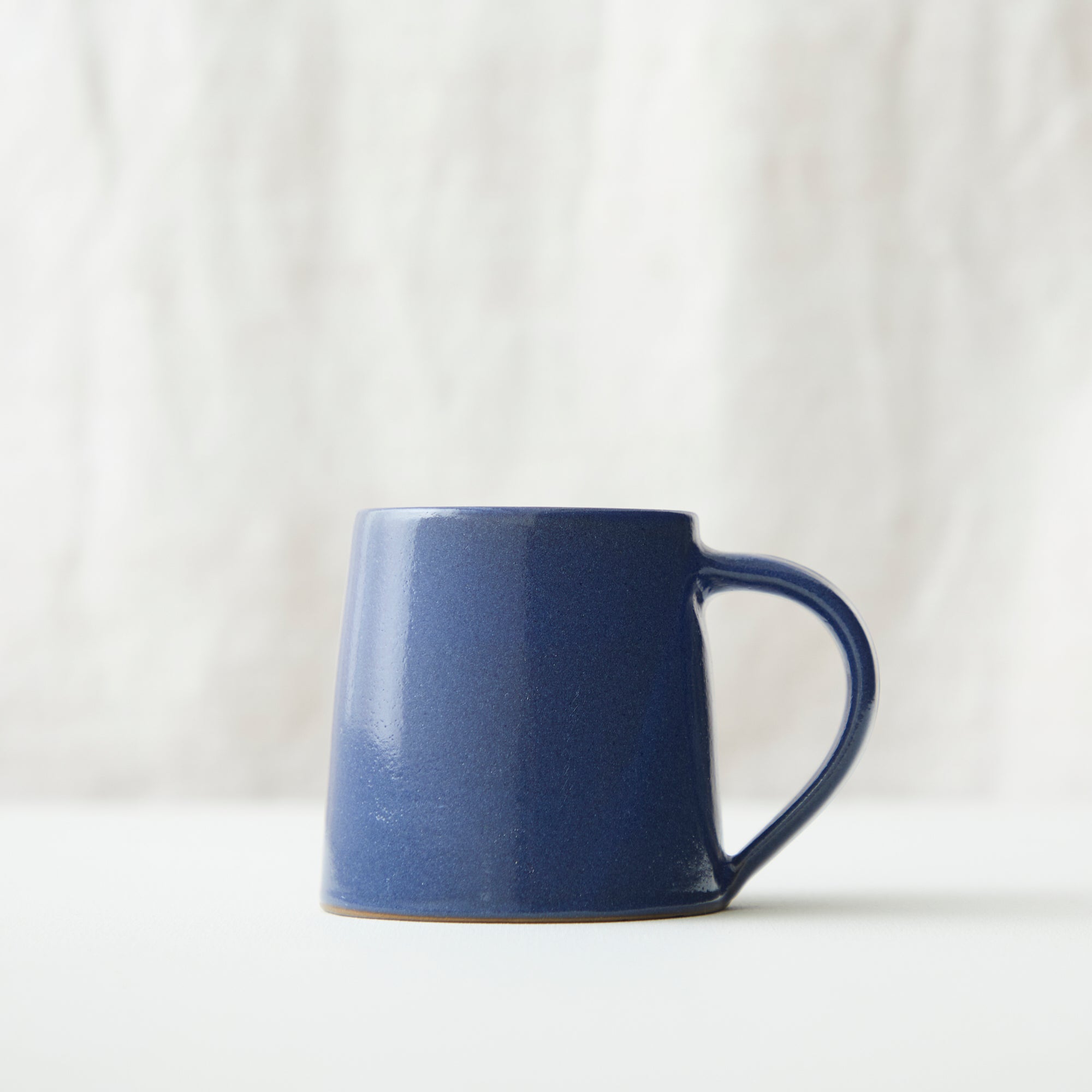 A dark blue ceramic mug with a slightly tapered body and a curved handle.