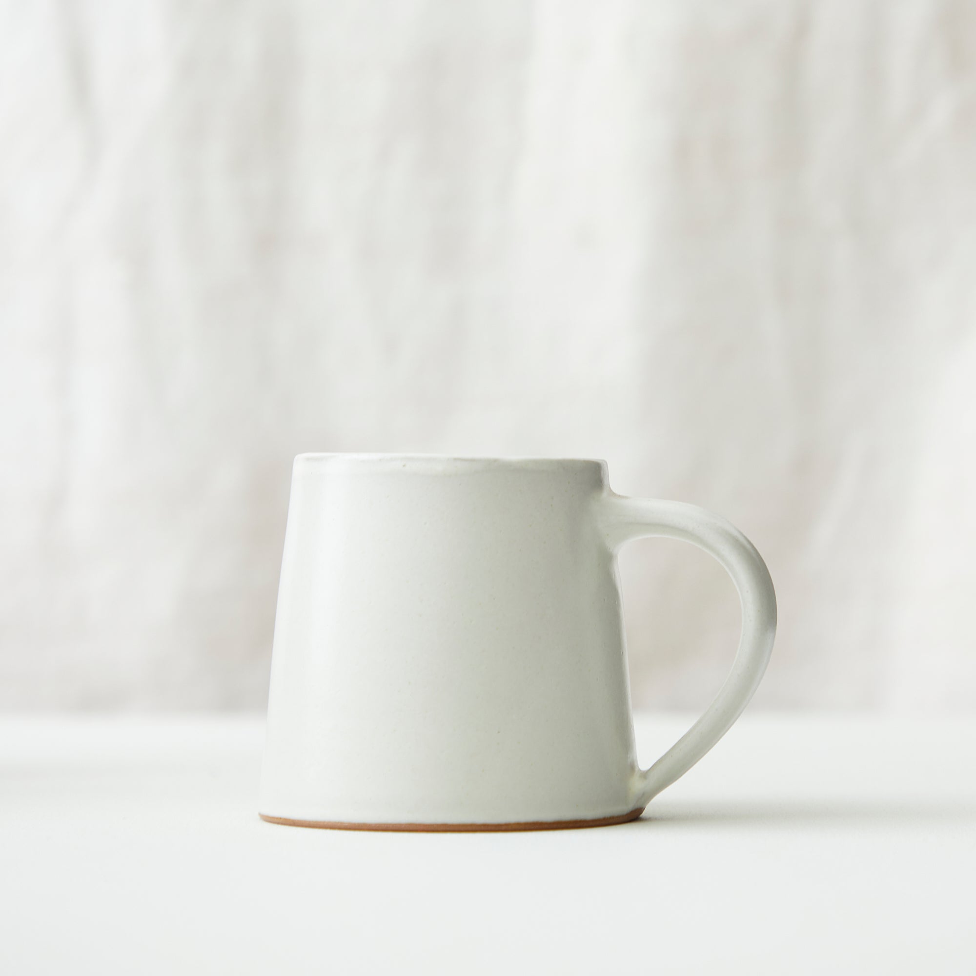 Off-white ceramic mug with a slightly tapered body and a curved handle.  The mug has a subtle, light brown rim.