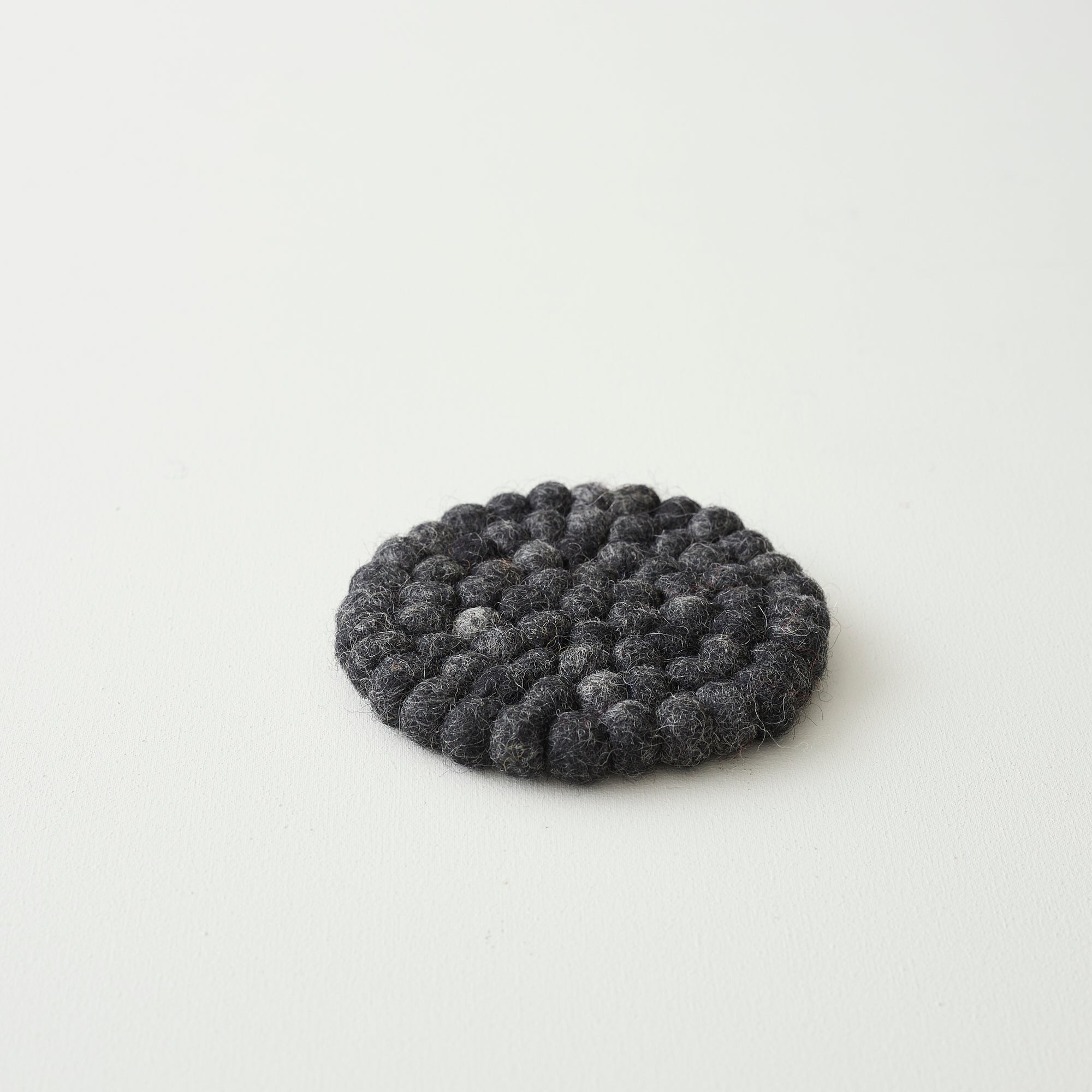 Dark gray round felt coaster made of small, densely packed wool balls.