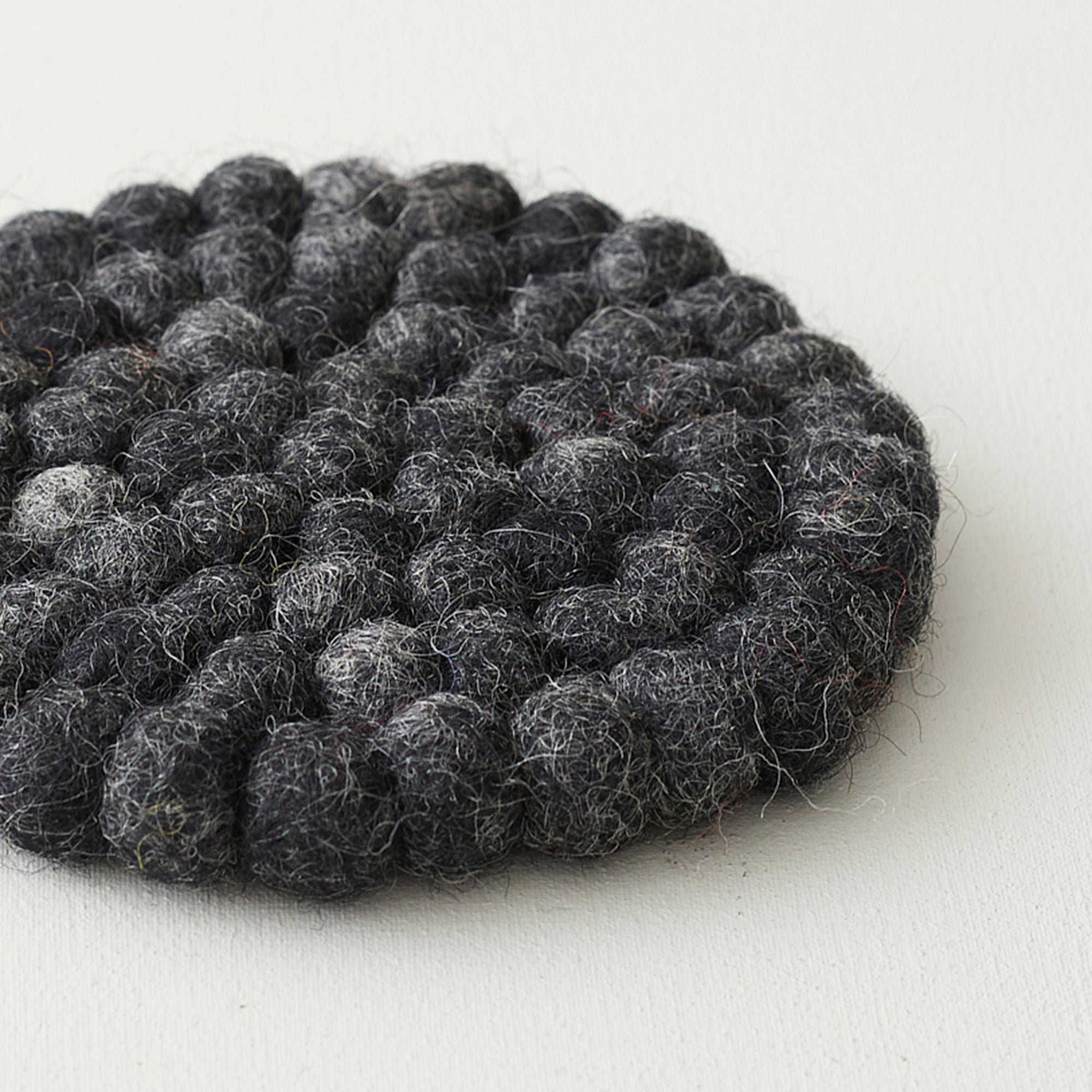 Dark gray round felt coaster with a textured surface of small, densely packed wool balls.