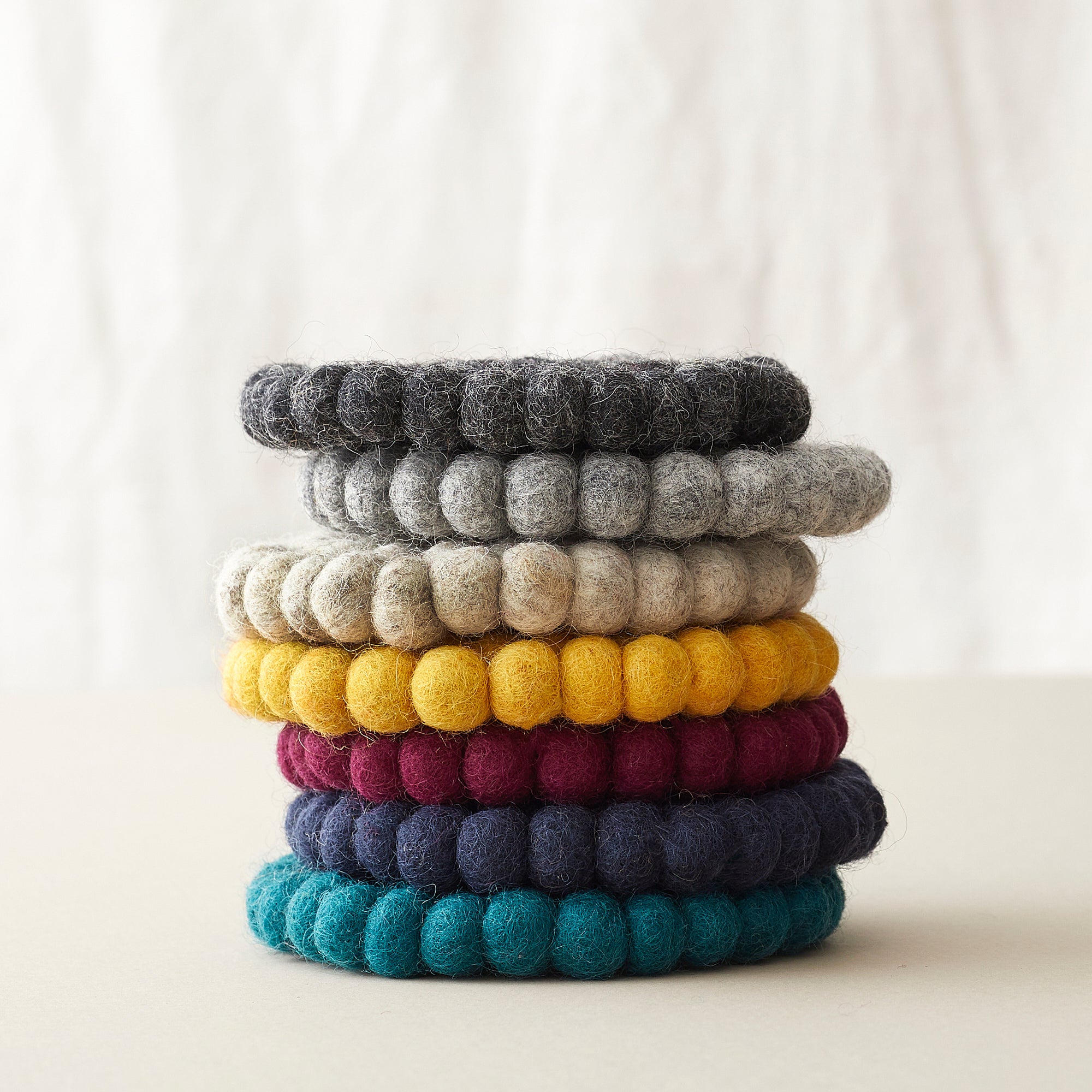 Stack of six round felt coasters in assorted colors; dark gray, light gray, mustard yellow, burgundy, navy blue, and teal.