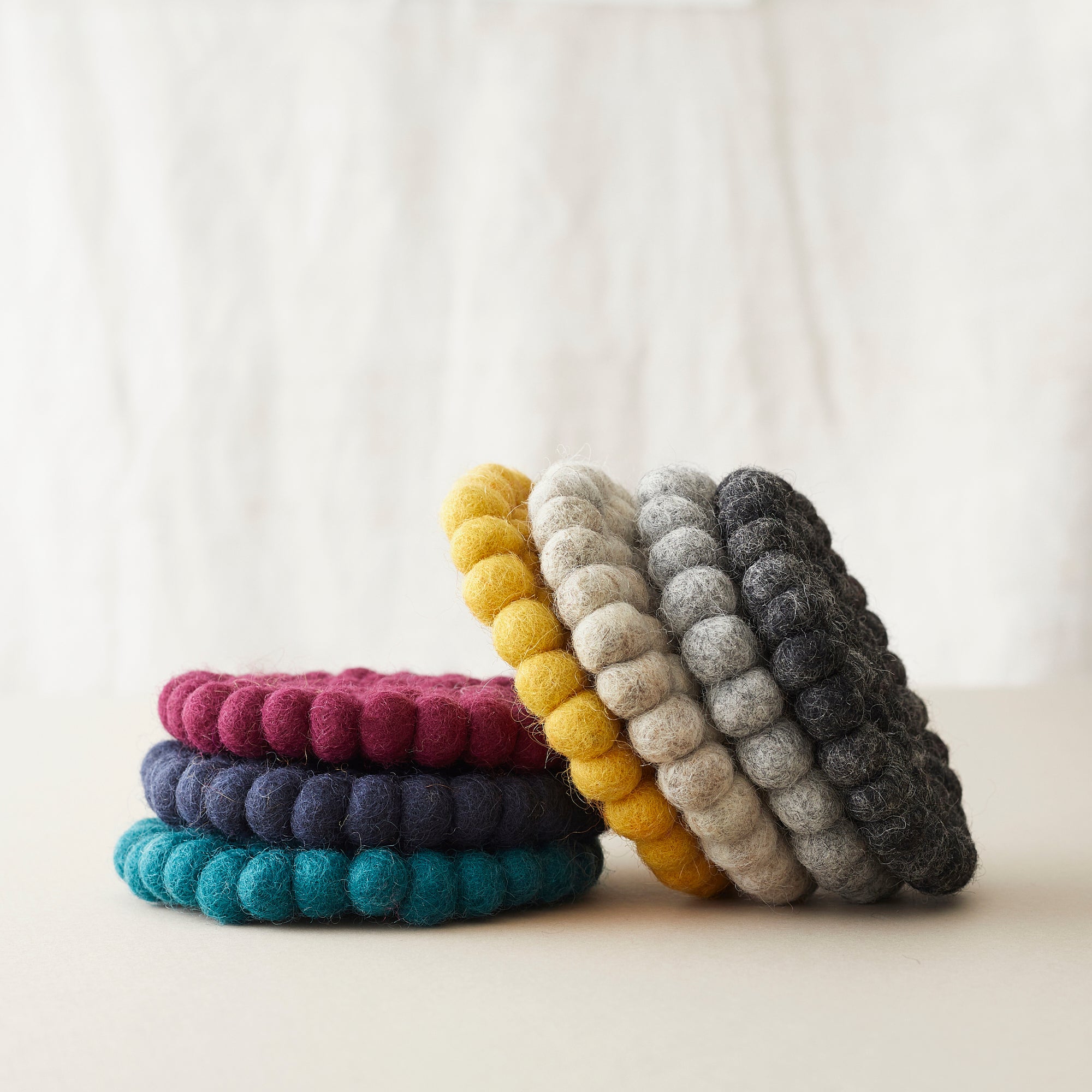 Stack of round felt coasters in teal, navy, burgundy, mustard, gray, and charcoal.