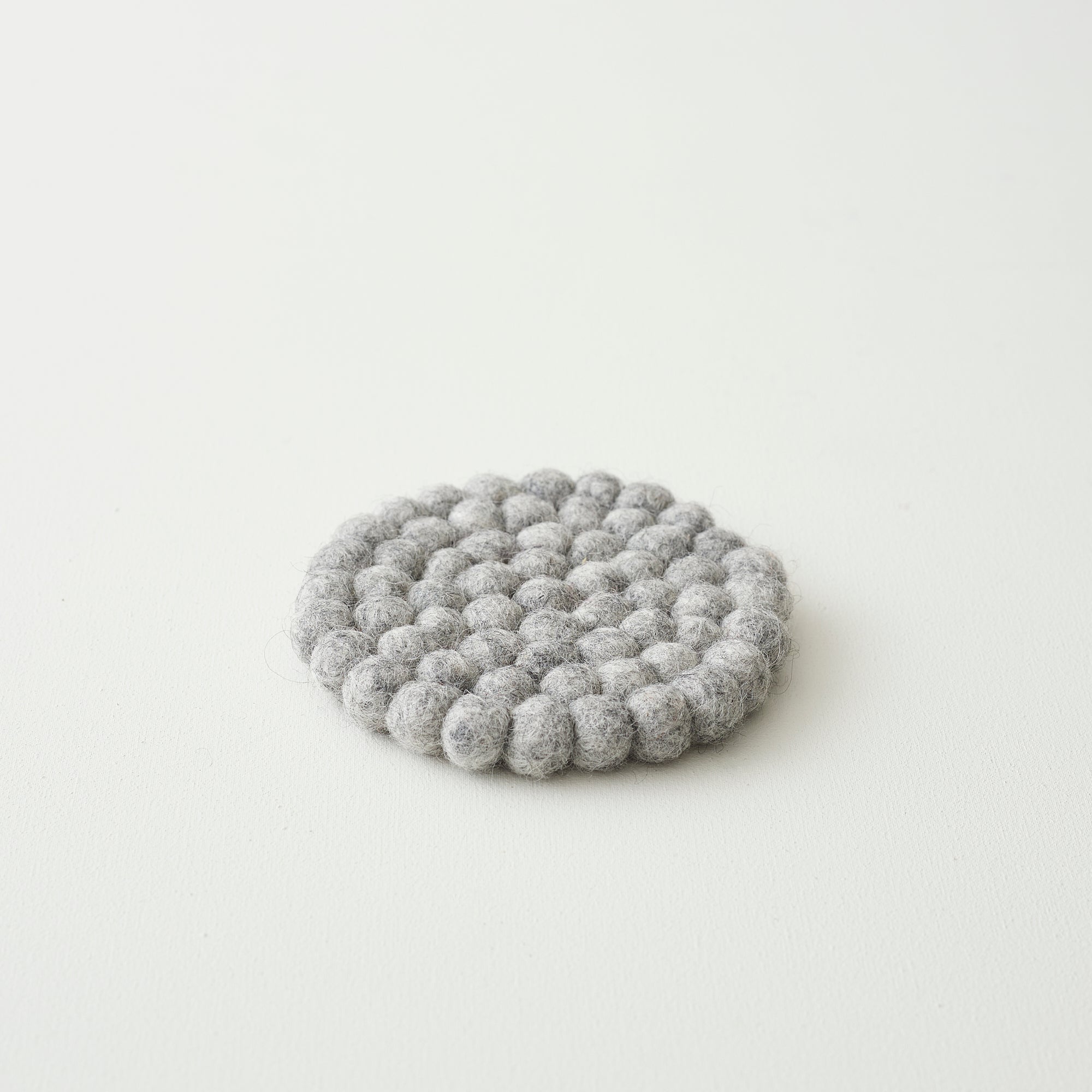 Round gray felt coaster made of small, densely packed balls of wool.