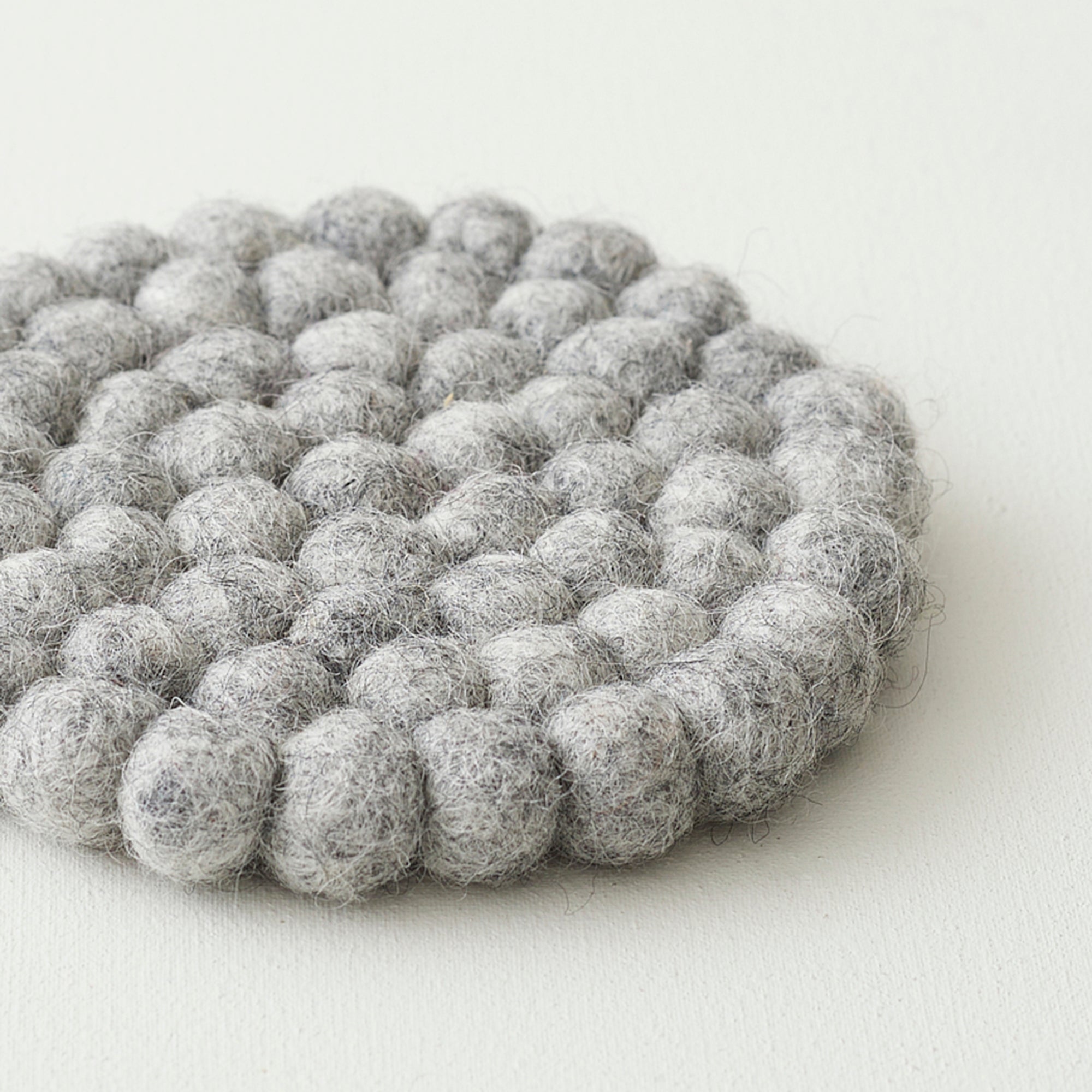 Round gray felt coaster made of densely packed small balls of wool.