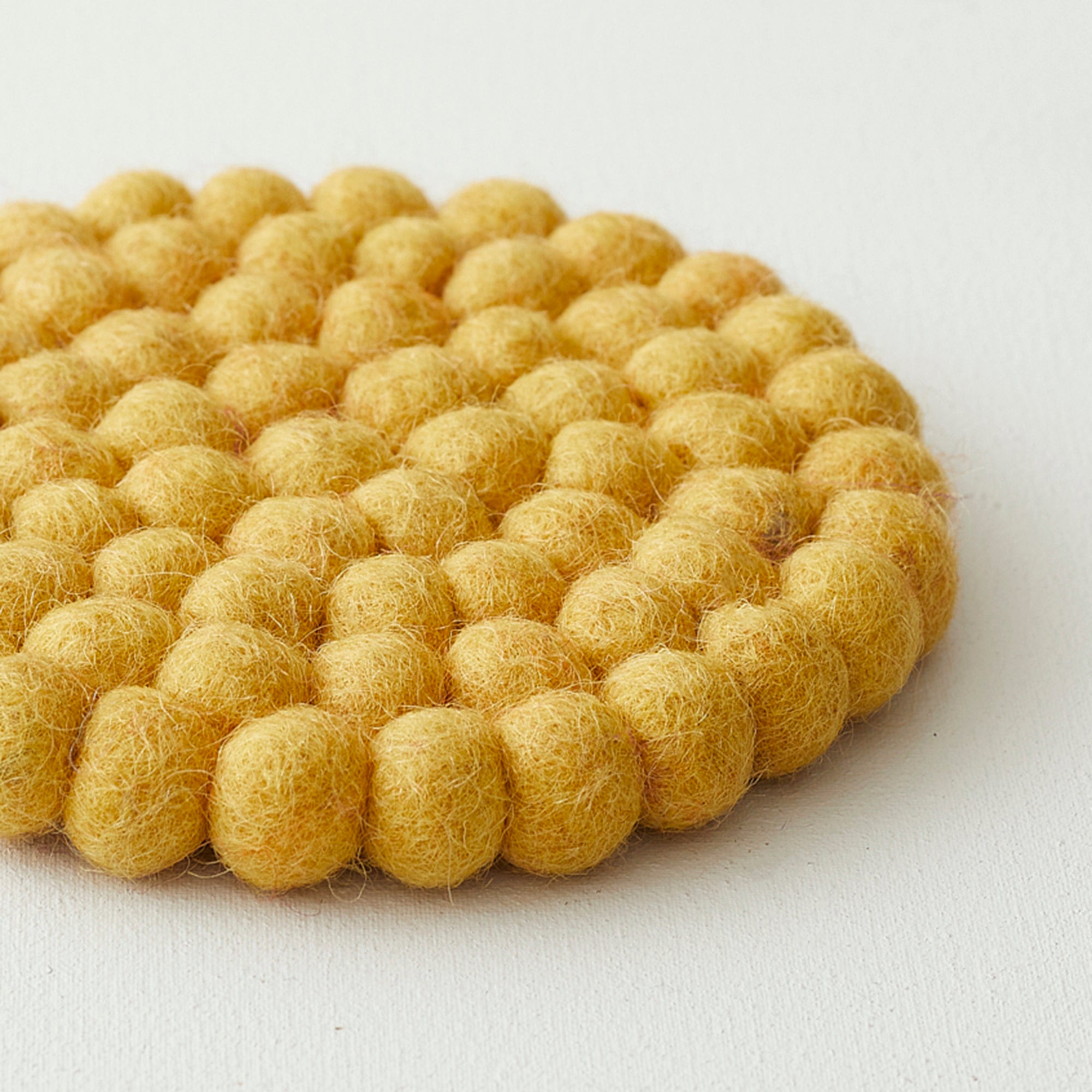 Round yellow felt coaster made of densely packed small balls of wool.