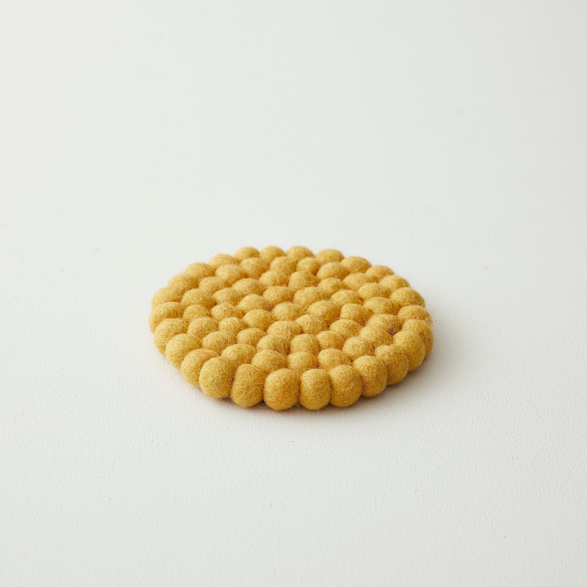 Round mustard yellow felt coaster composed of small, densely packed balls.