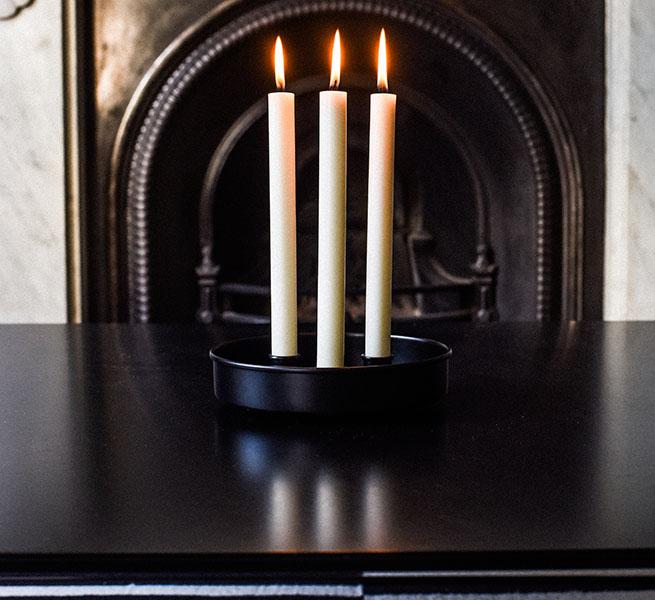 Three cream-colored candles burning in a black metal candle holder on a dark surface.