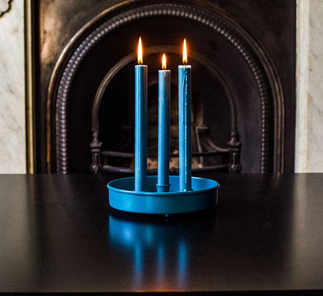 Teal three-candle holder with lit teal candles on a dark surface.
