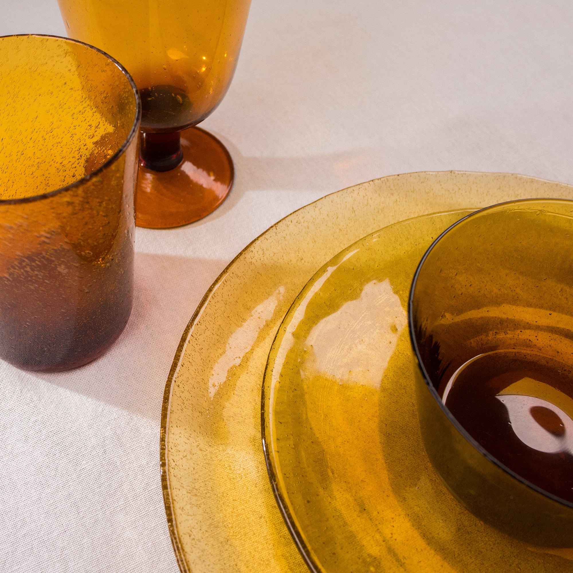 Amber glass dinnerware set:  a large plate, smaller plate, bowl, and tumbler, all with a textured surface.