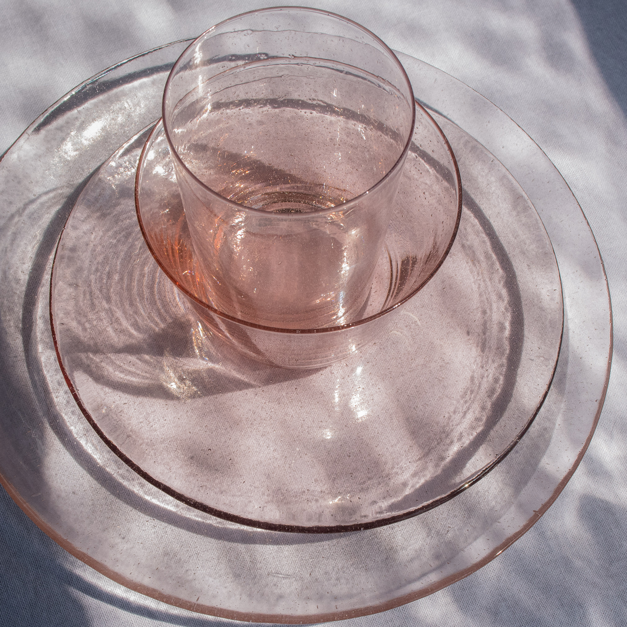 Pink glass tumbler nestled in a set of similarly colored, subtly textured glass plates.