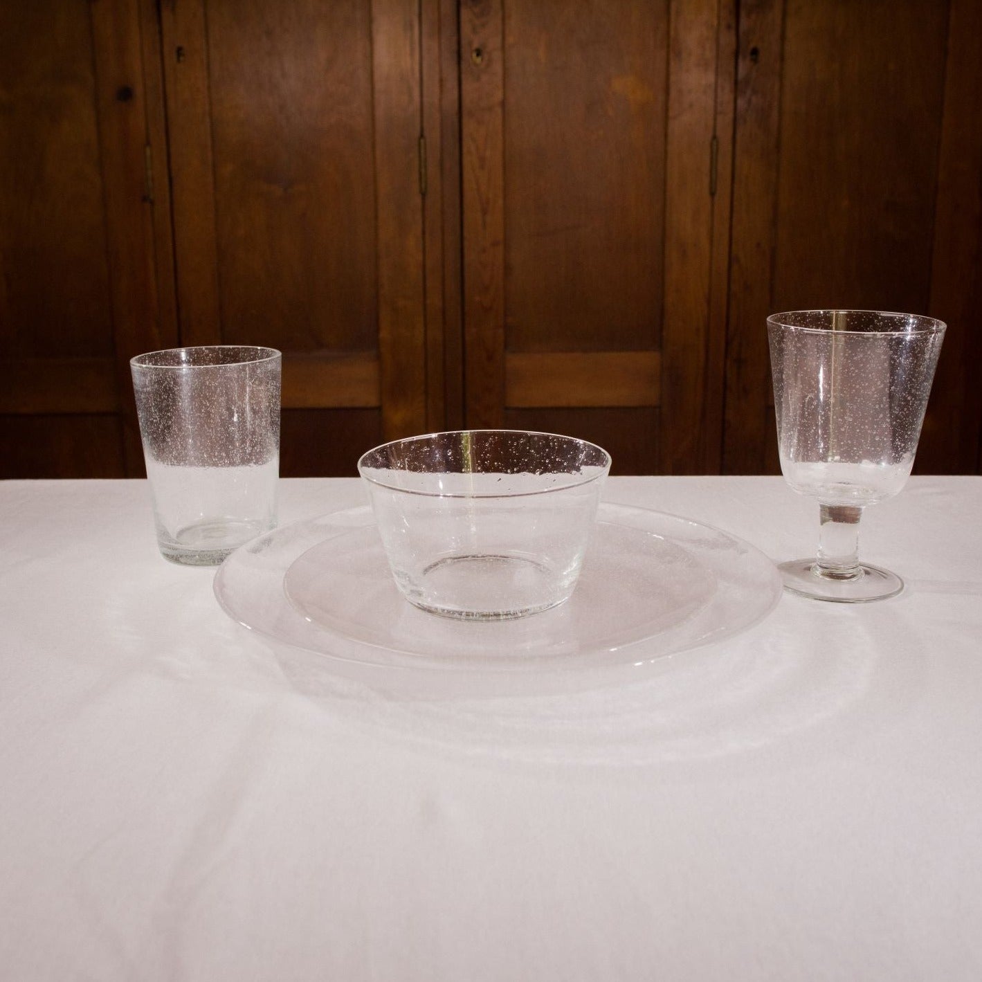 Set of clear bubble glass tableware: tumbler, bowl, and stemmed glass on a plate.