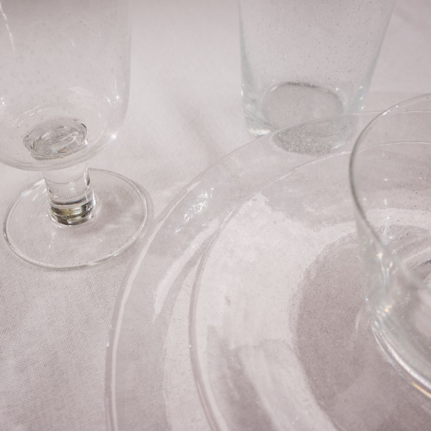 Clear glass dinnerware set: a stemmed glass, tumbler, and large plate with a textured surface.