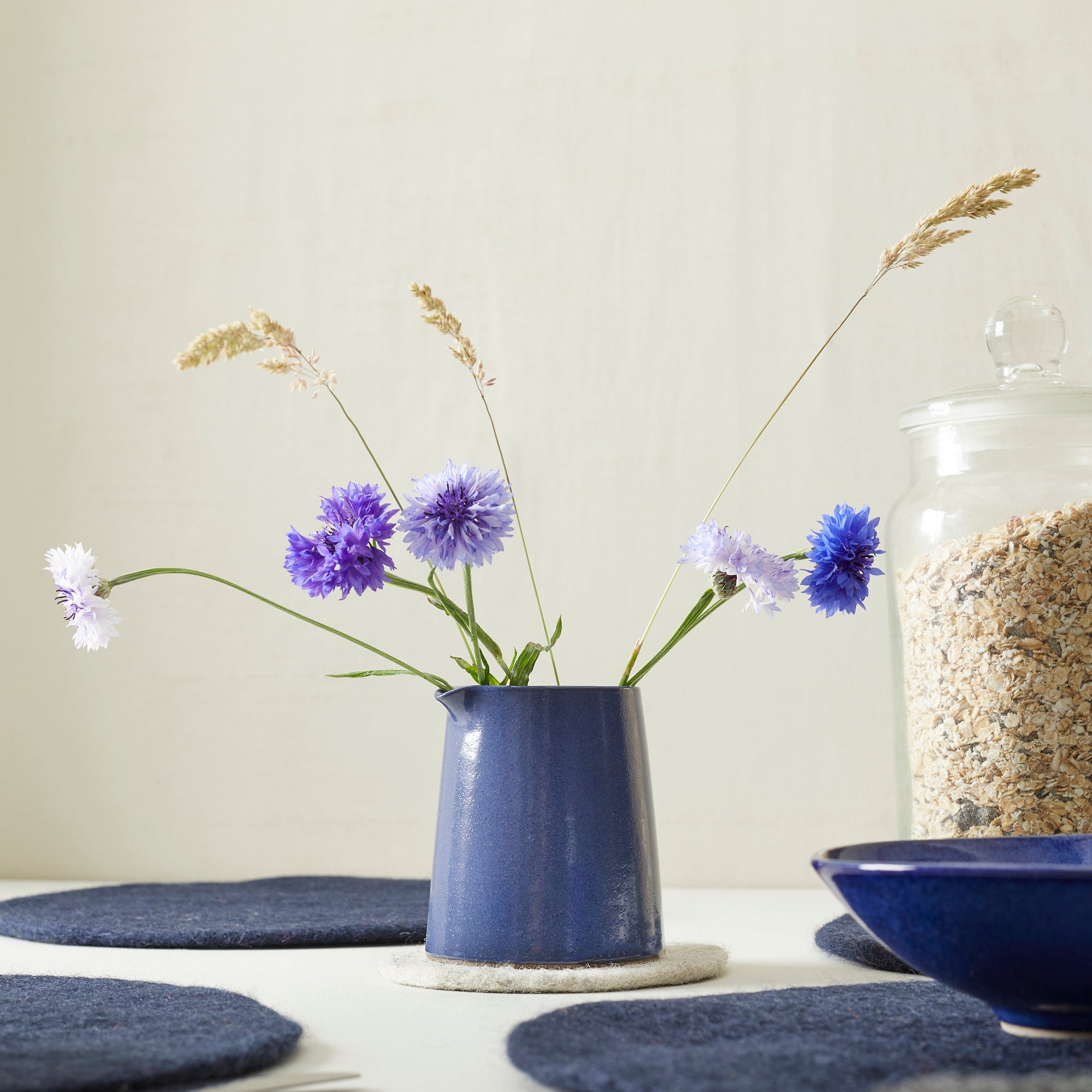 Blue ceramic creamer holding purple and white cornflowers and dried grasses.