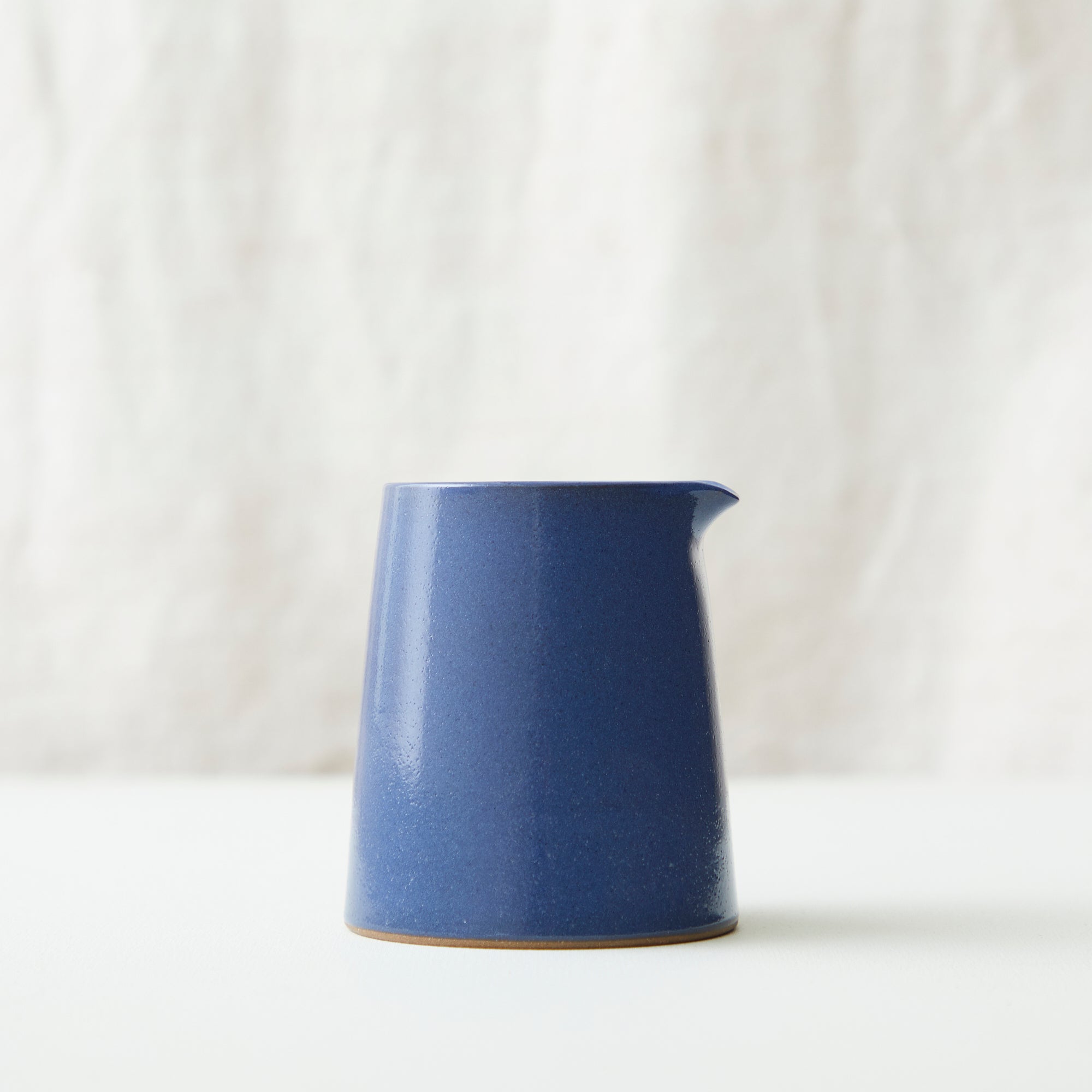 A small, dark blue ceramic creamer with a slightly textured surface and a light brown rim.