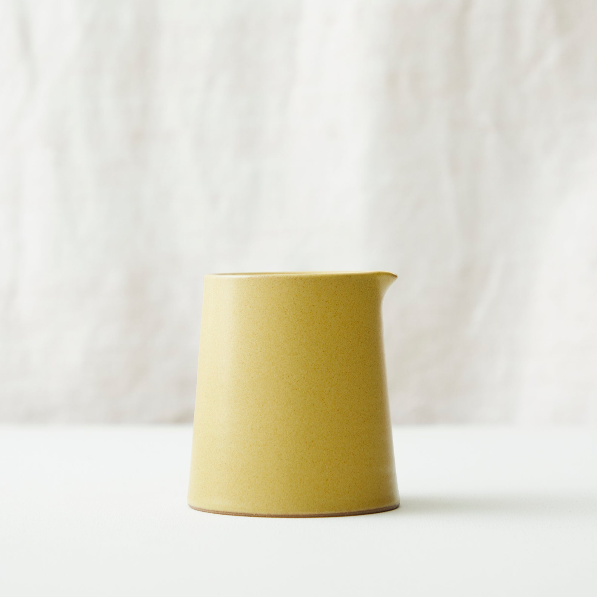 Mustard yellow ceramic creamer with a slightly tapered body and a small spout.