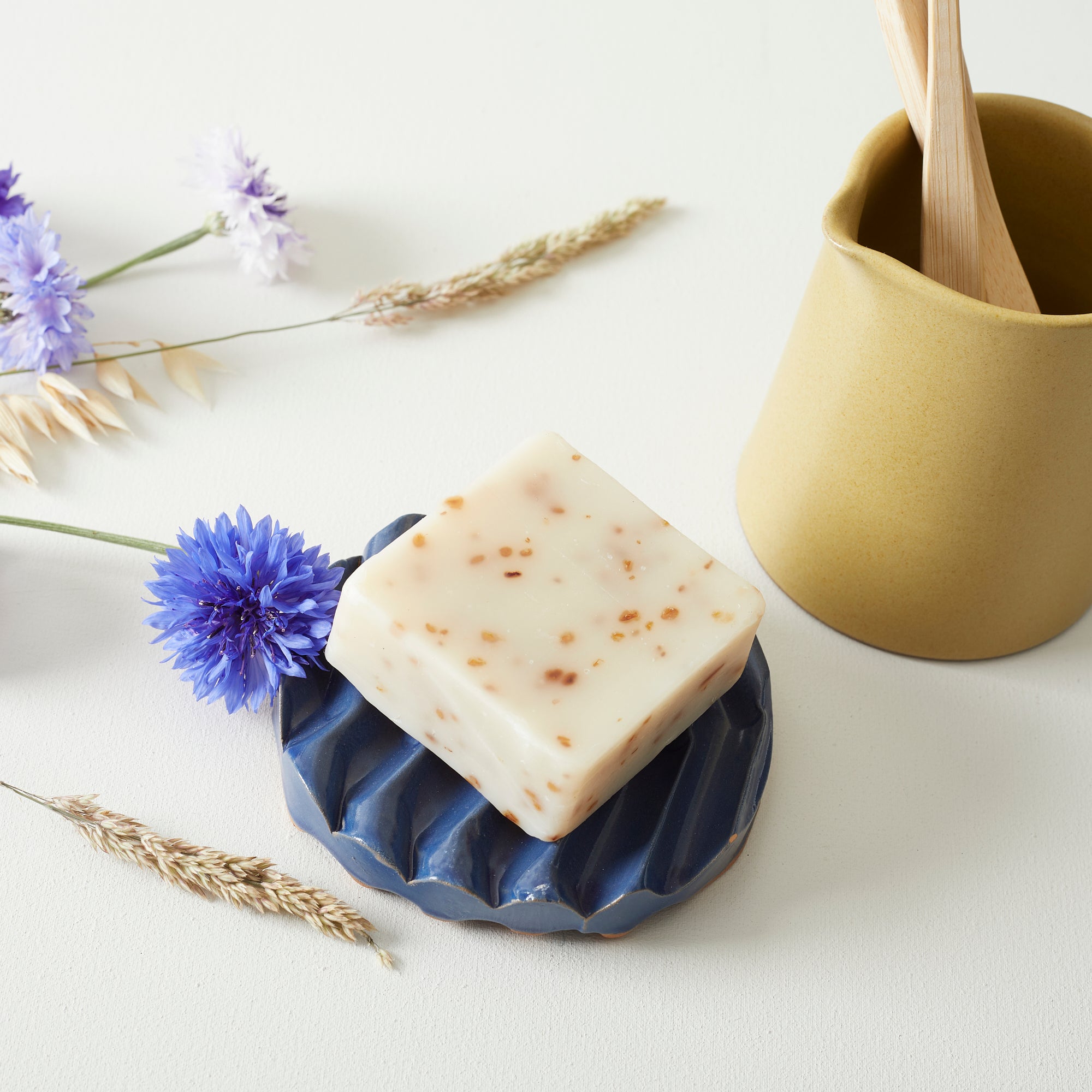 Off-white bar soap with flecks of brown, resting on a blue ceramic soap dish.